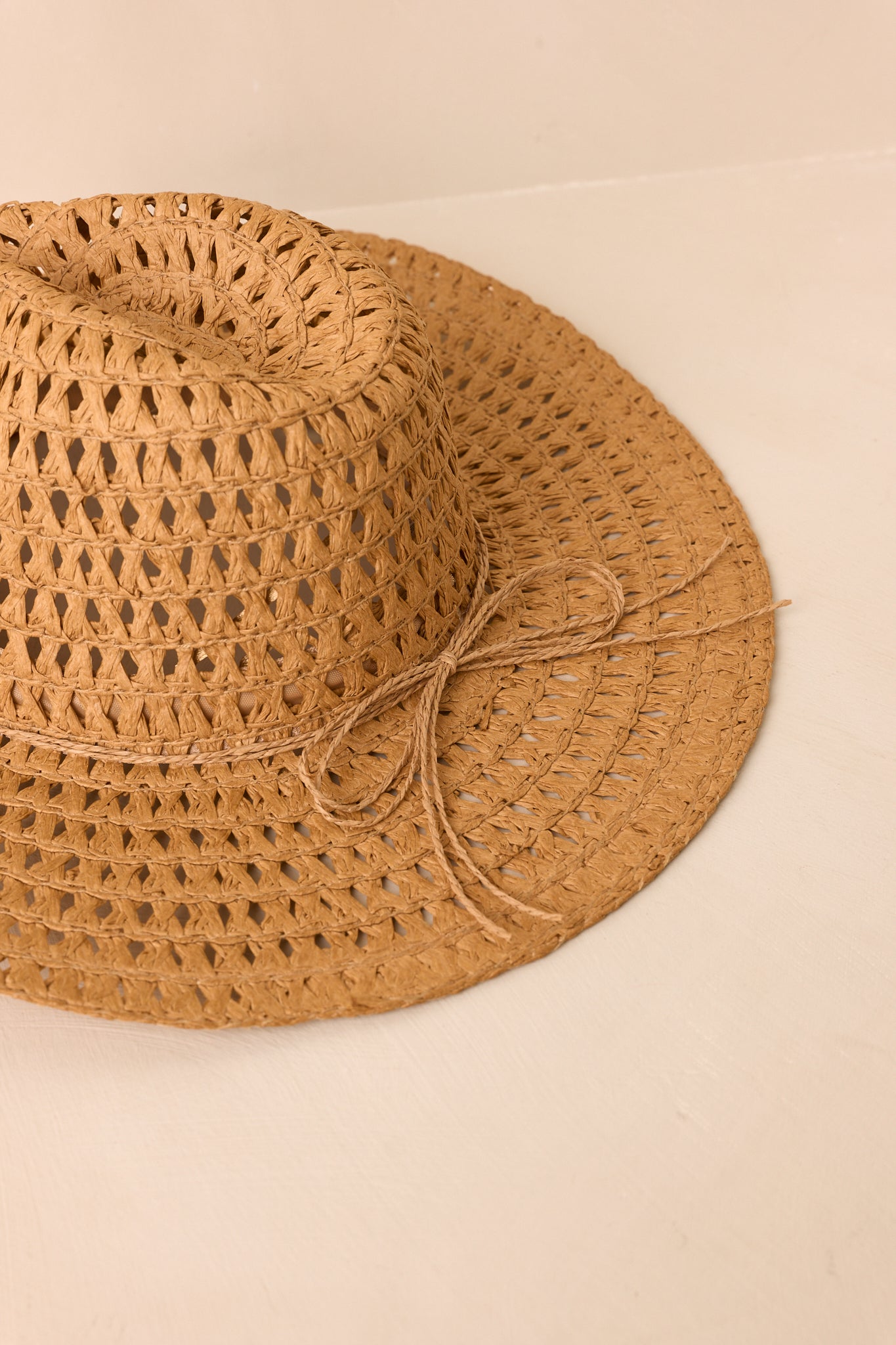 Open-weave straw hat highlighting its wide brim and relaxed textured silhouette on a beige backdrop.