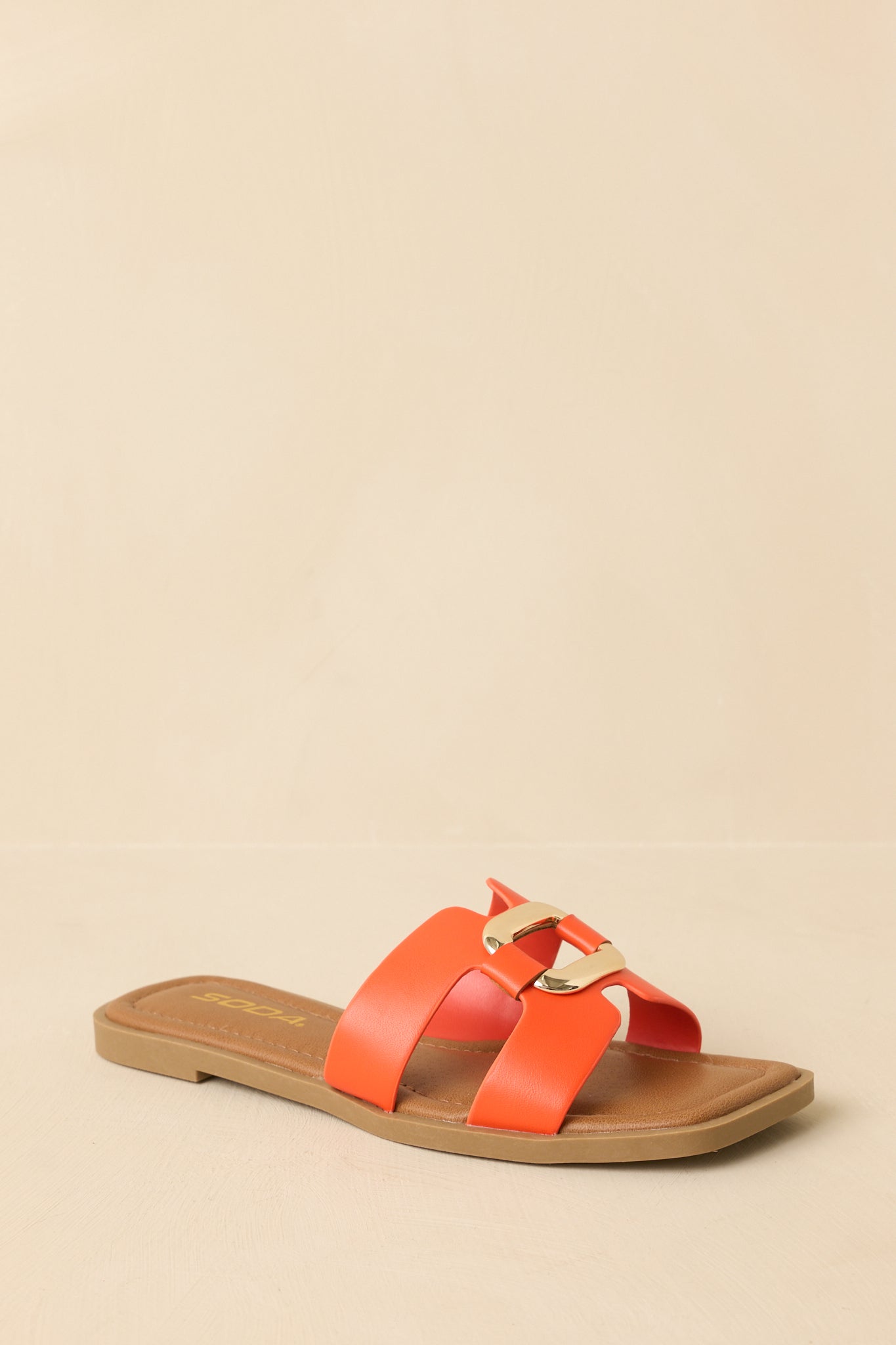 Angled view of the orange faux-leather slide sandals on a neutral beige backdrop highlighting the lightly cushioned footbed.