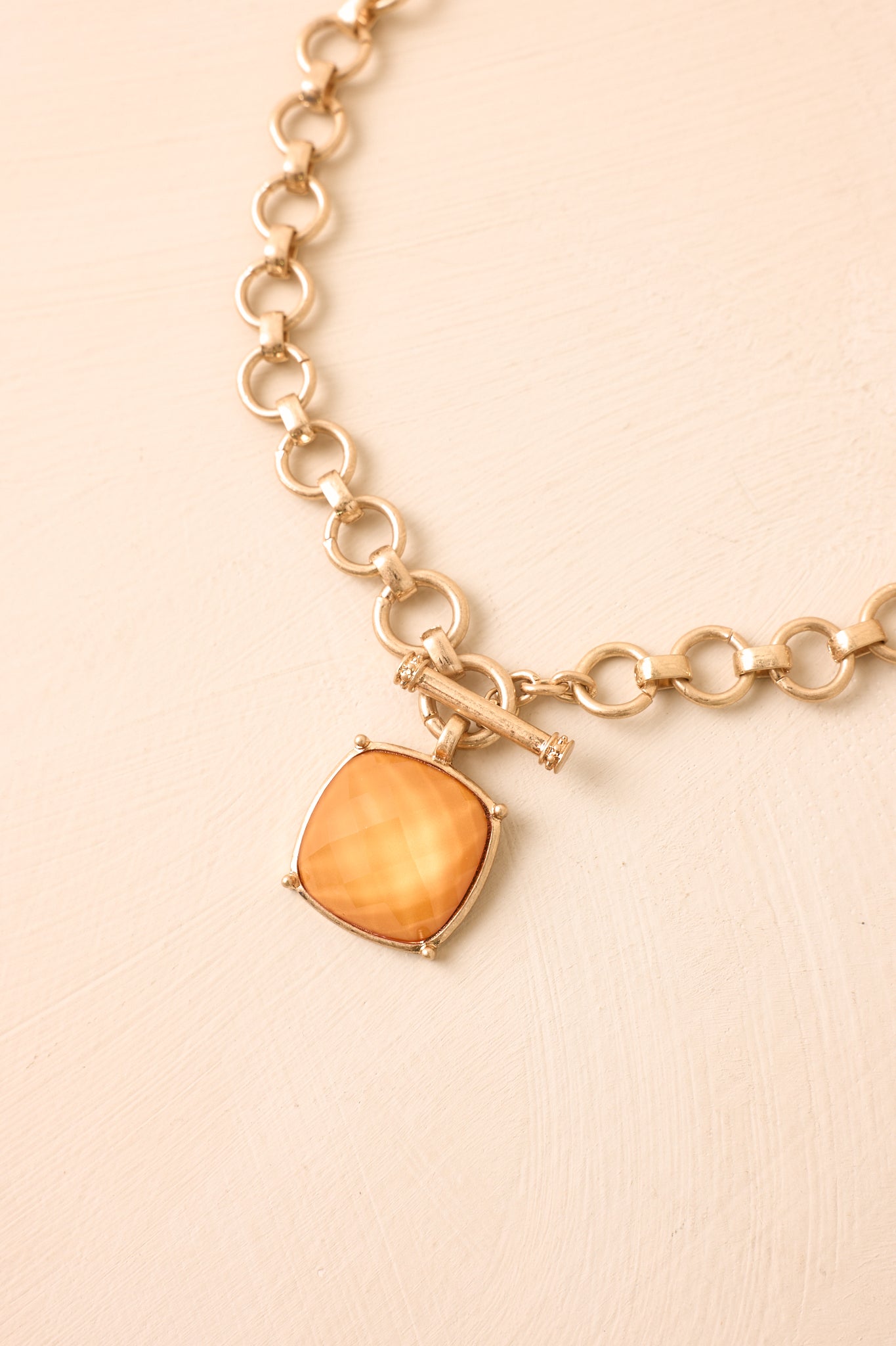 Orange pendant necklace with circular gold links and a polished square setting presented on a neutral backdrop.