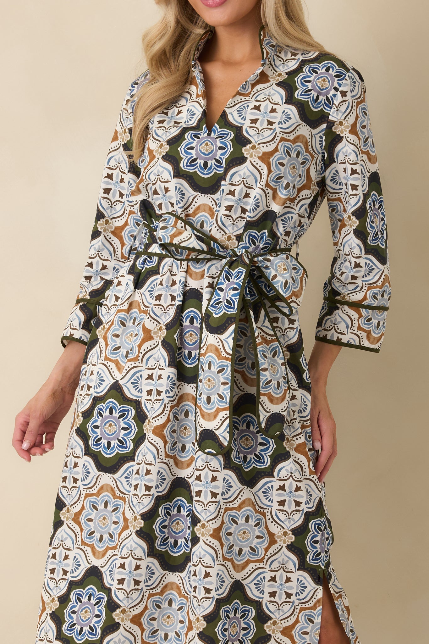 Close-up of an ornate medallion print maxi dress featuring a stand collar, split V-neckline, olive piping, and tie belt.