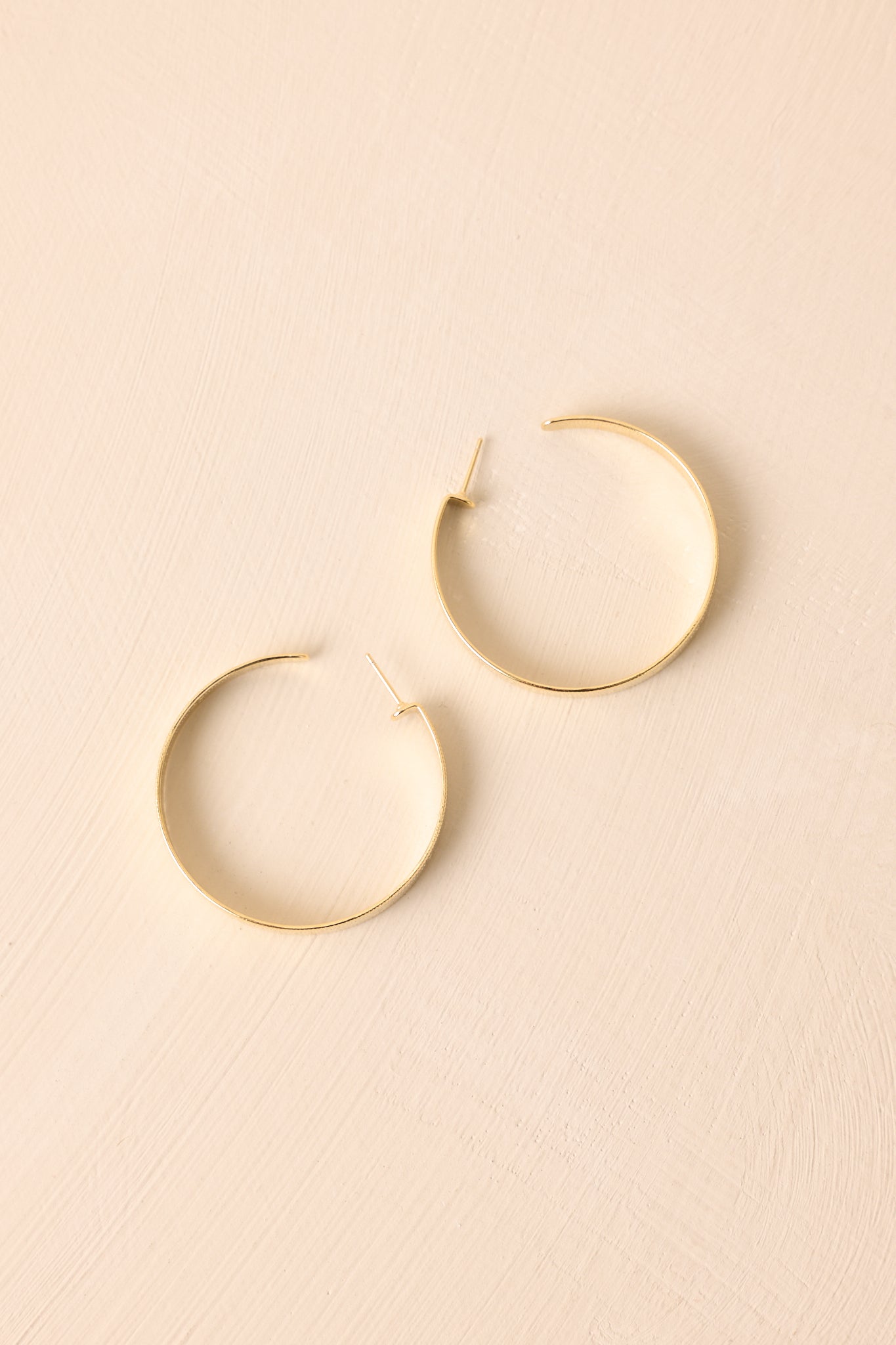 An overhead shot of the gold earrings showcasing their incomplete hoop shape and overall size.