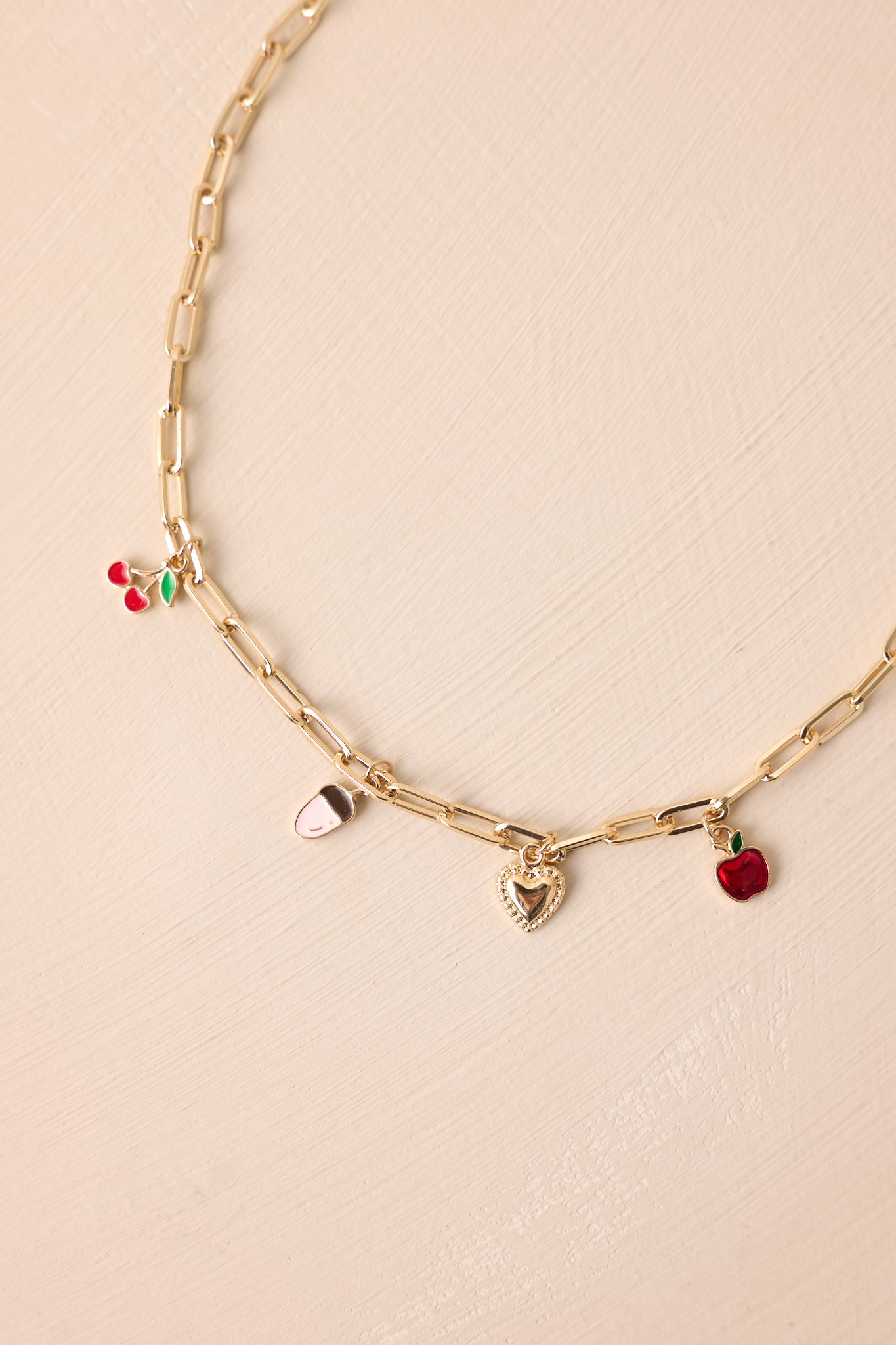 Overhead view emphasizing the charms’ placement, including the red apple, heart, and cherry, on the rectangular gold chain.