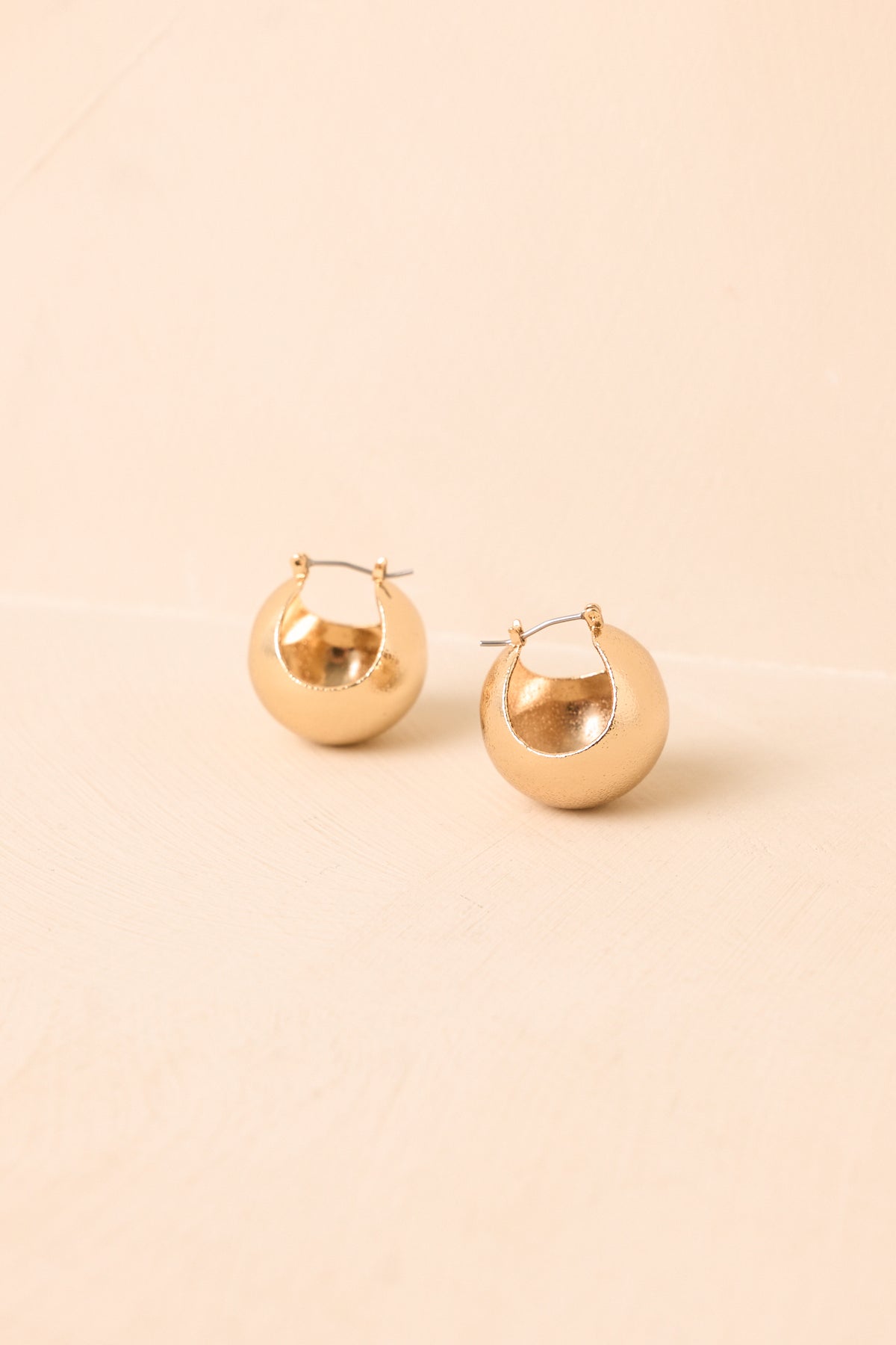 Oversized gold-tone round studs displaying their dimensional shape and softly textured finish.
