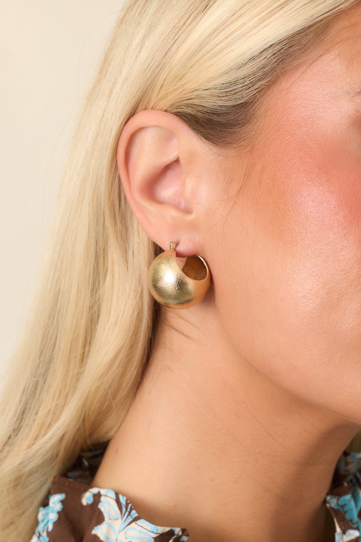 Oversized round gold-tone stud earrings feature a softly textured surface and sculptural shape.