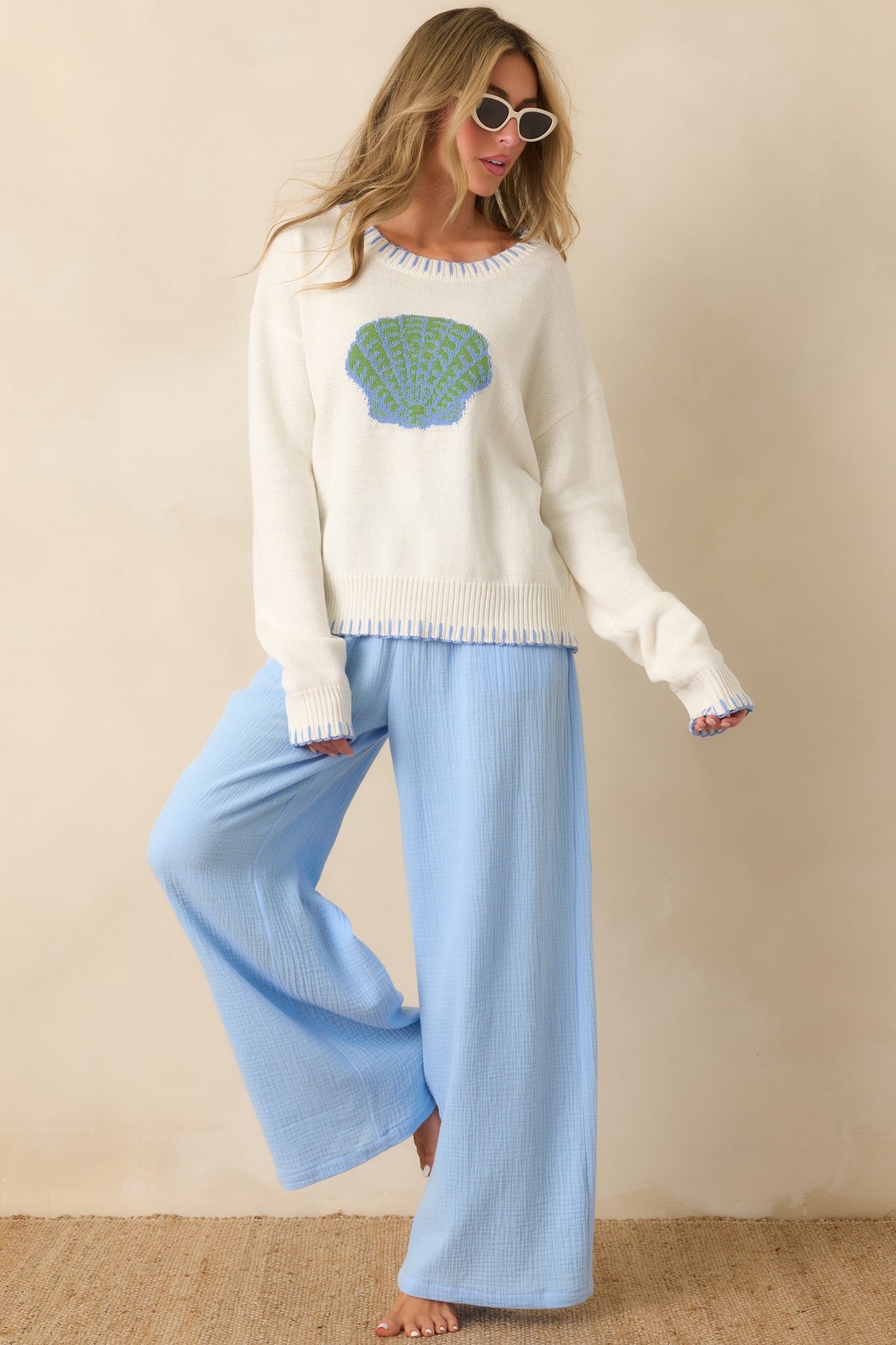 Classic white knit sweater featuring ribbed trim, long sleeves, and a front shell motif.