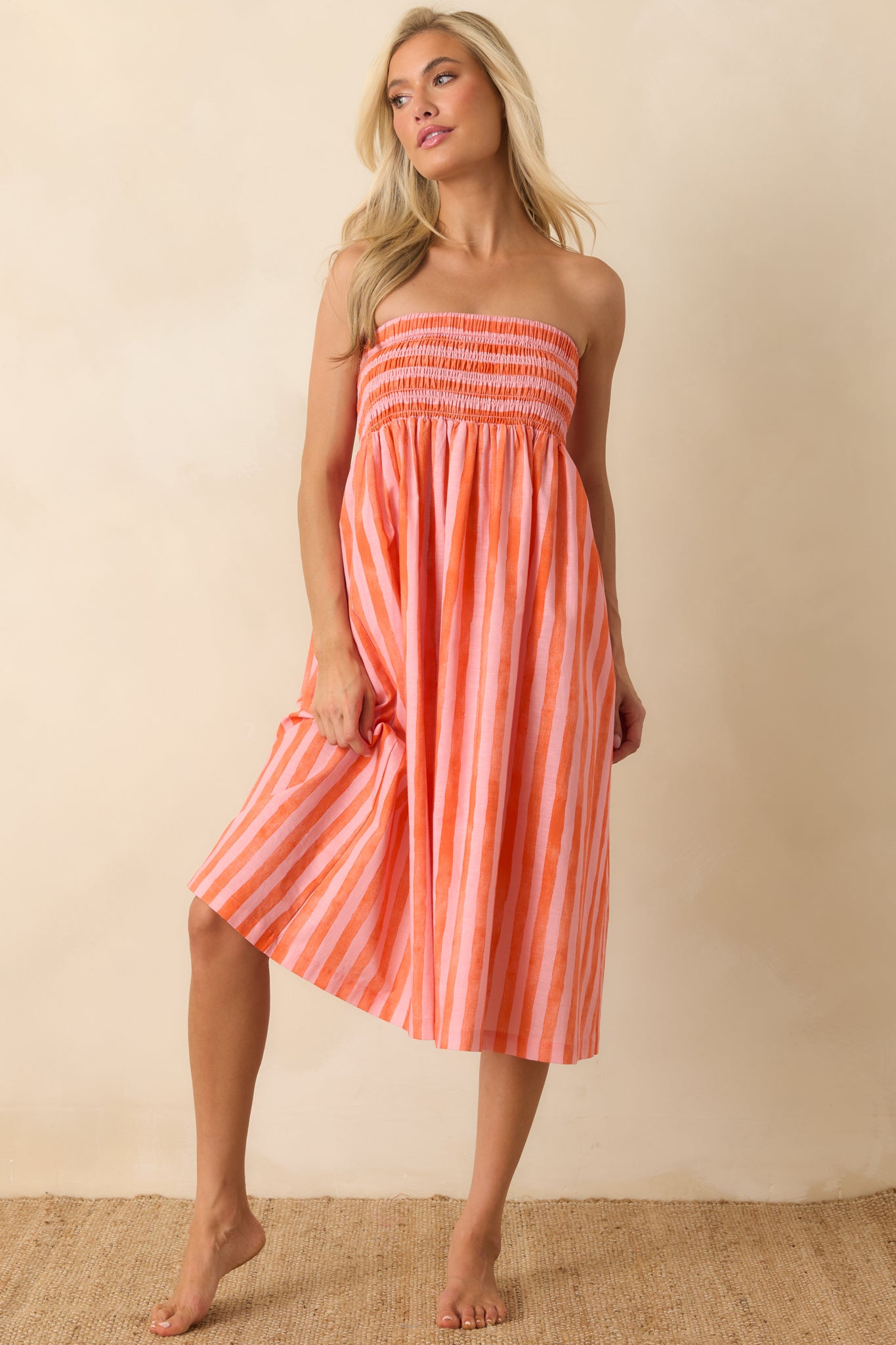 Pink and orange striped dress featuring a fitted smocked bodice and an easy, breathable midi-length shape.