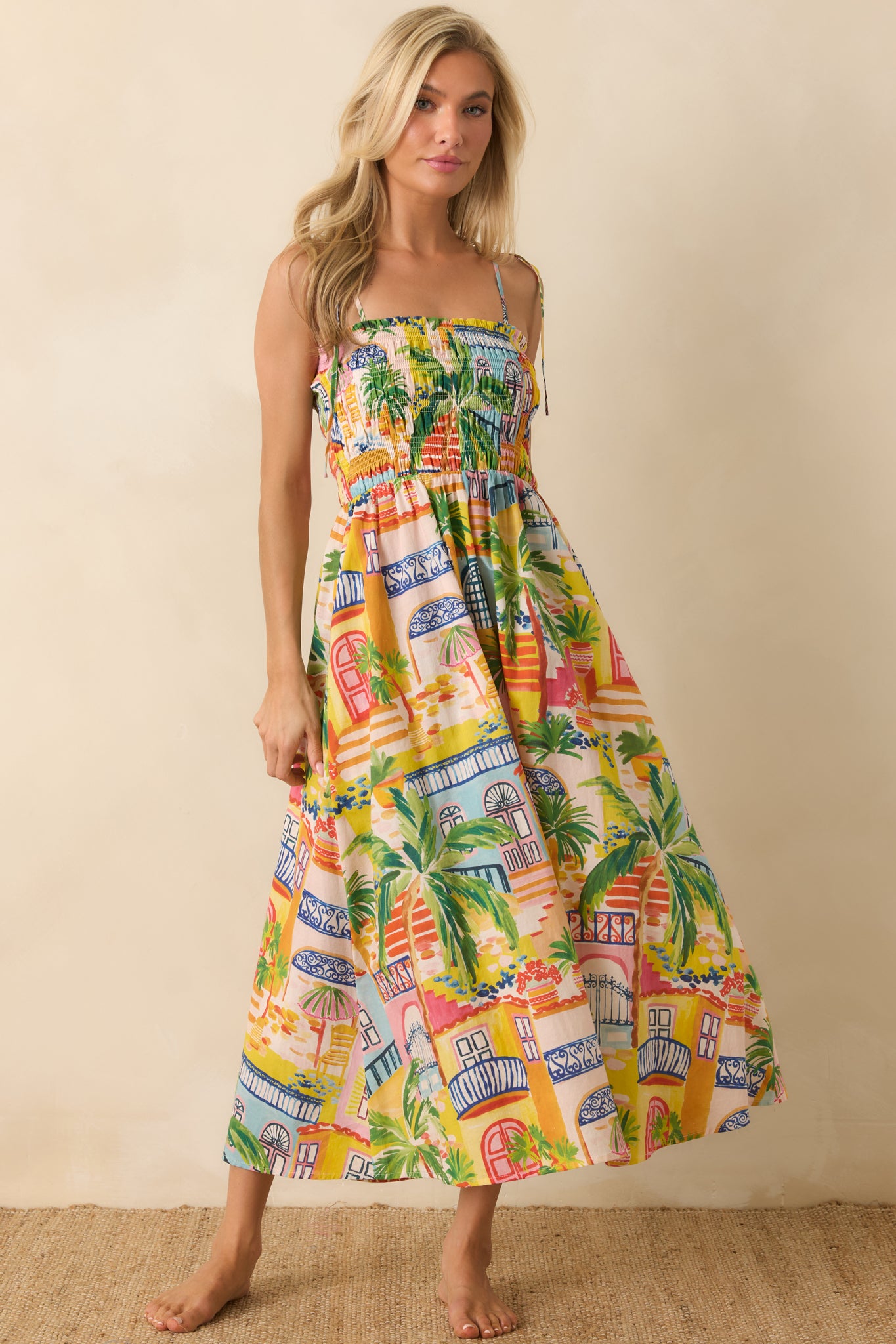 Cotton midi dress with a vibrant coastal village print, breezy silhouette, side pockets, and adjustable tie shoulders.