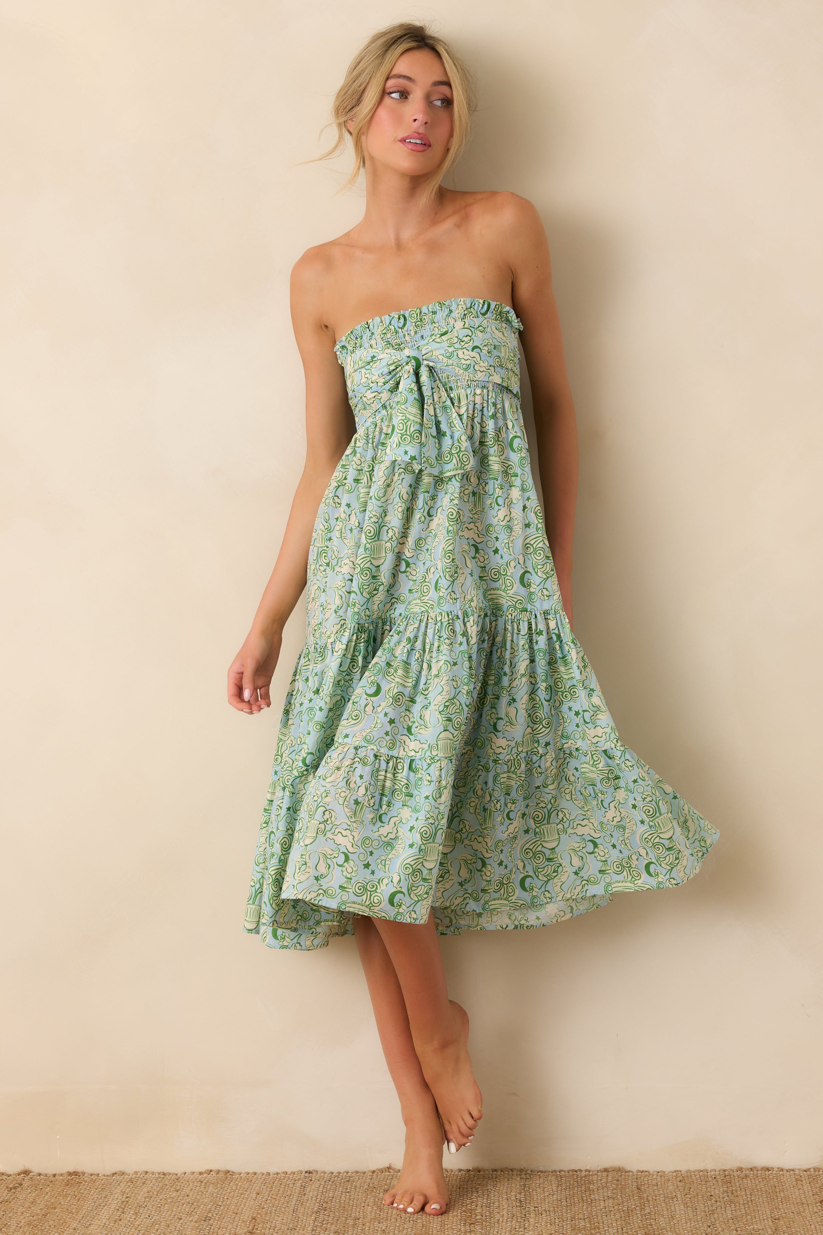 Woman wearing a strapless green mermaid print dress against a beige wall. Dress is smocked at top.