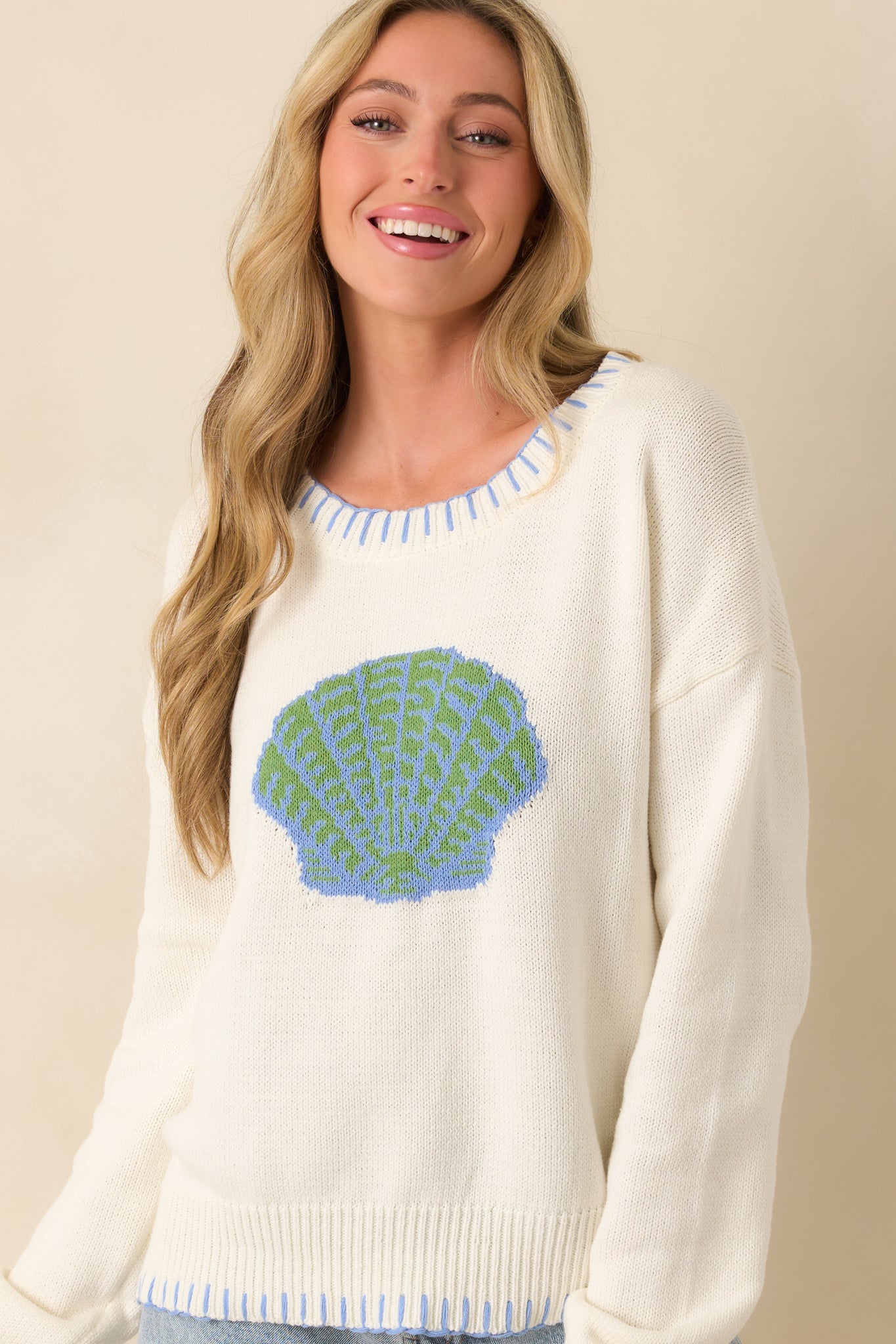 Front crop showing long sleeves and ribbed trim with whipstitch detailing on white knit sweater.
