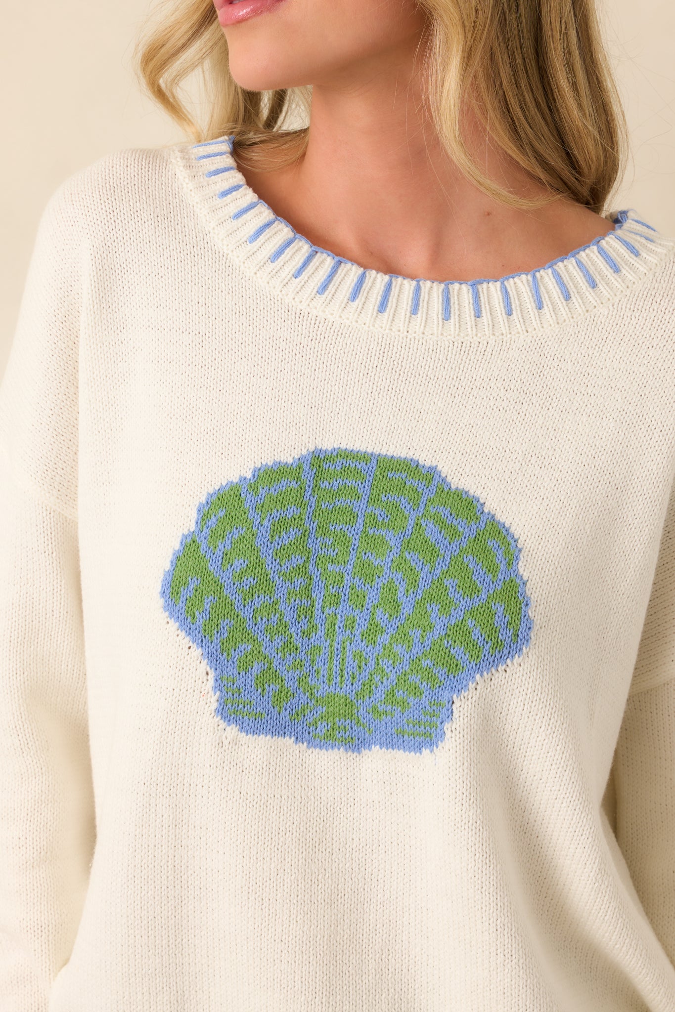 Close-up of white knit sweater showing shell graphic, ribbed trim, and whipstitch detailing.