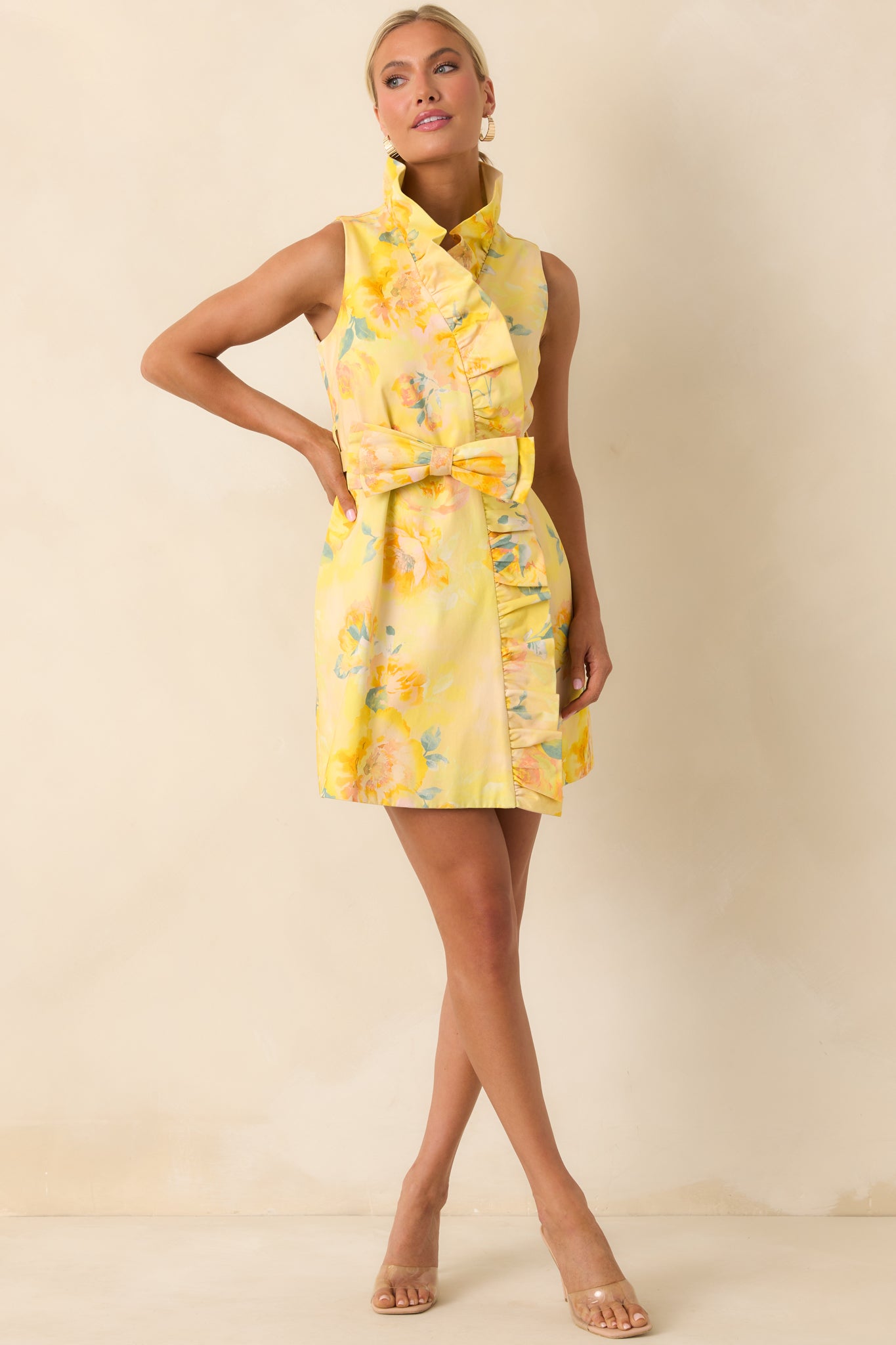 Yellow floral mini dress with ruffled collar, faux wrap silhouette, and tie waist creating a softly defined shape.