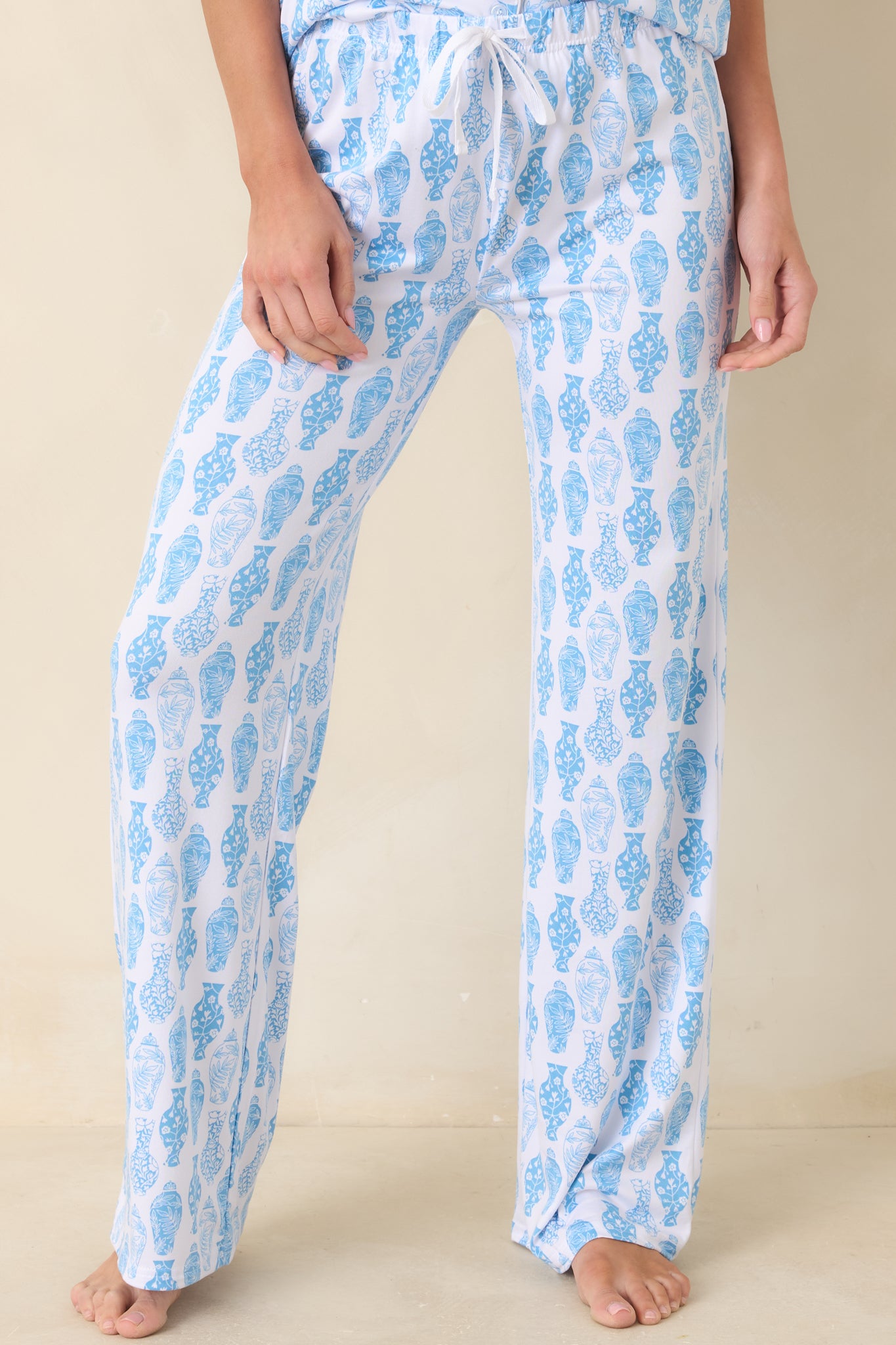 Mid-section close-up of pajama pants showing elastic waistband, drawstring tie, and detailed blue print on white fabric.