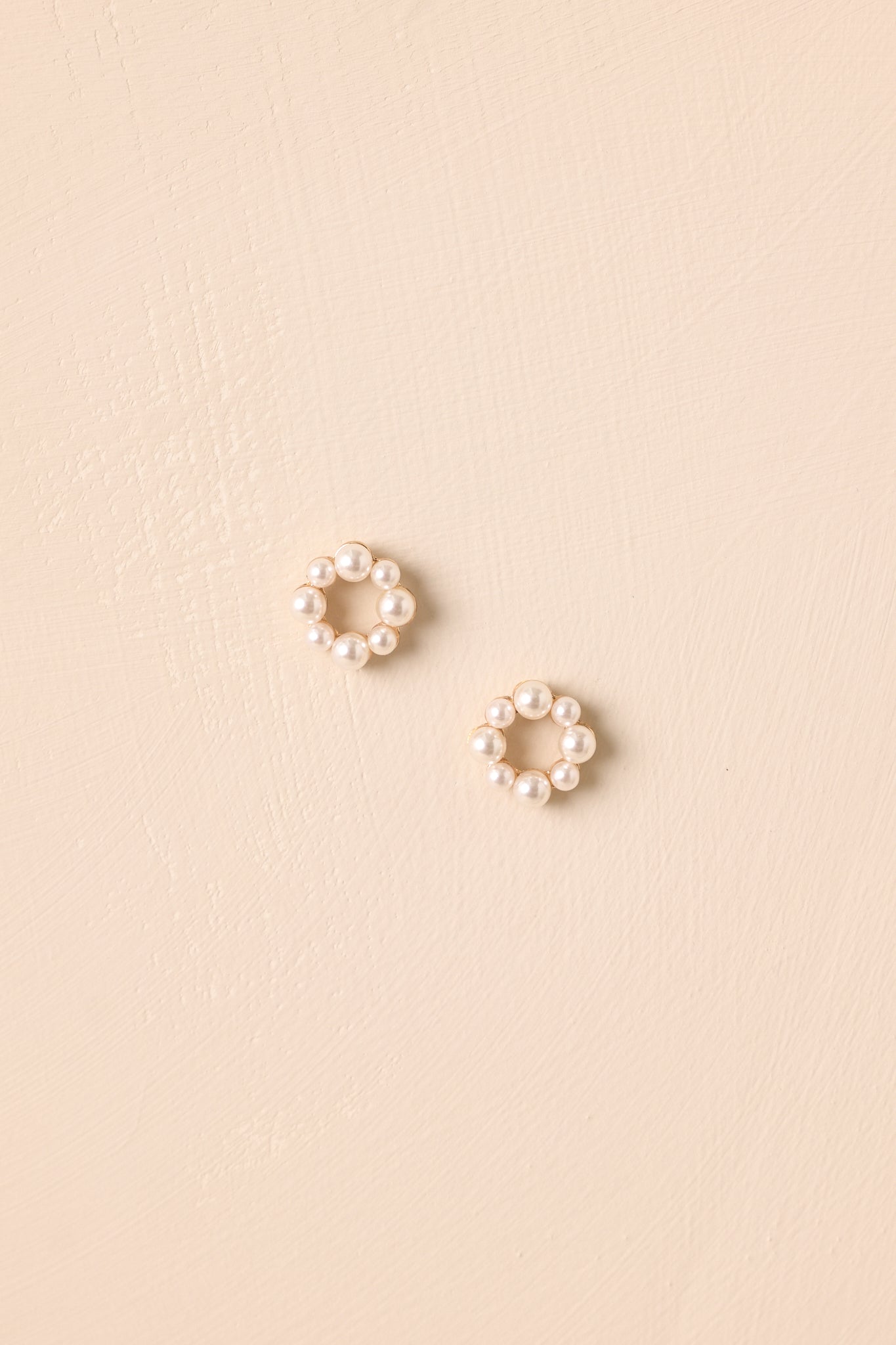 Pair of pearl-edged hoop earrings displayed on a beige backdrop.