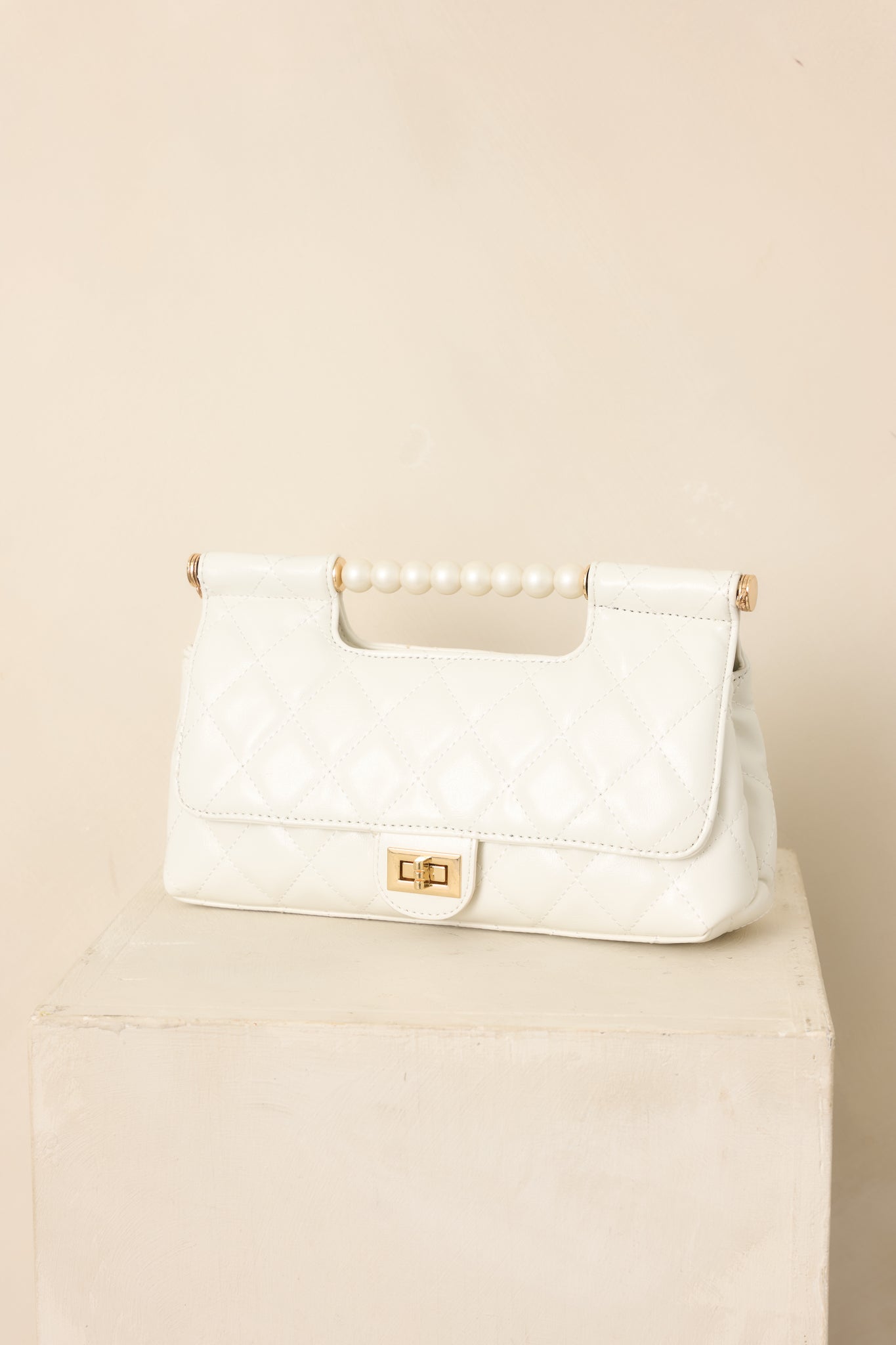 Faux leather handbag highlighting the rounded pearl top handle, gold-tone turn lock, and smooth structured finish.