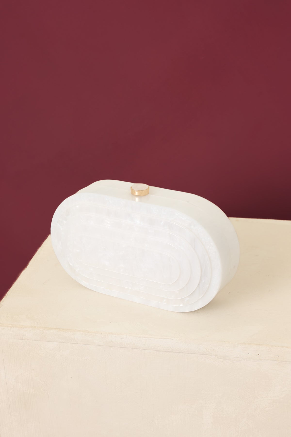 White pearlescent clutch highlighting its smooth, luminous finish and structured oval design with a refined top clasp closure.