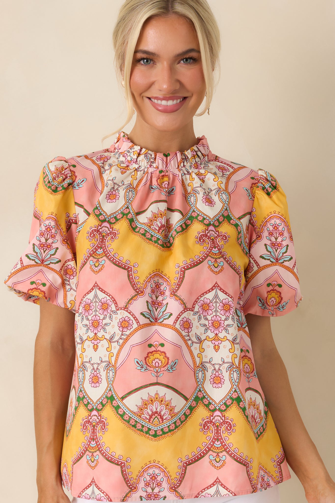 Pink and marigold print top highlighting the ruffled mock neckline and detailed ornamental scarf-print artwork.