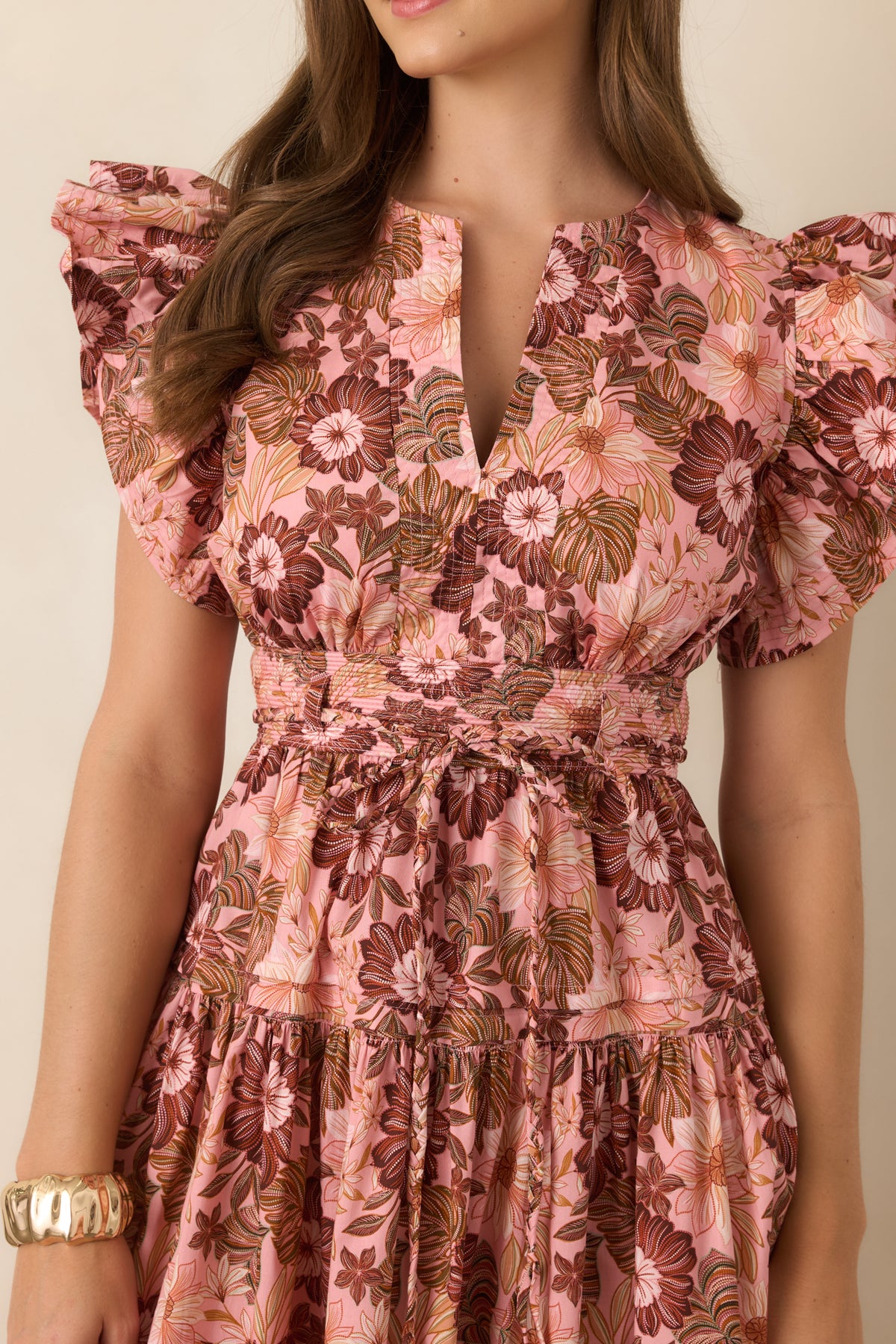 Close-up of the pastel pink and brown floral print, highlighting the V-neckline, delicate ruffle sleeve, and defined waist detailing.