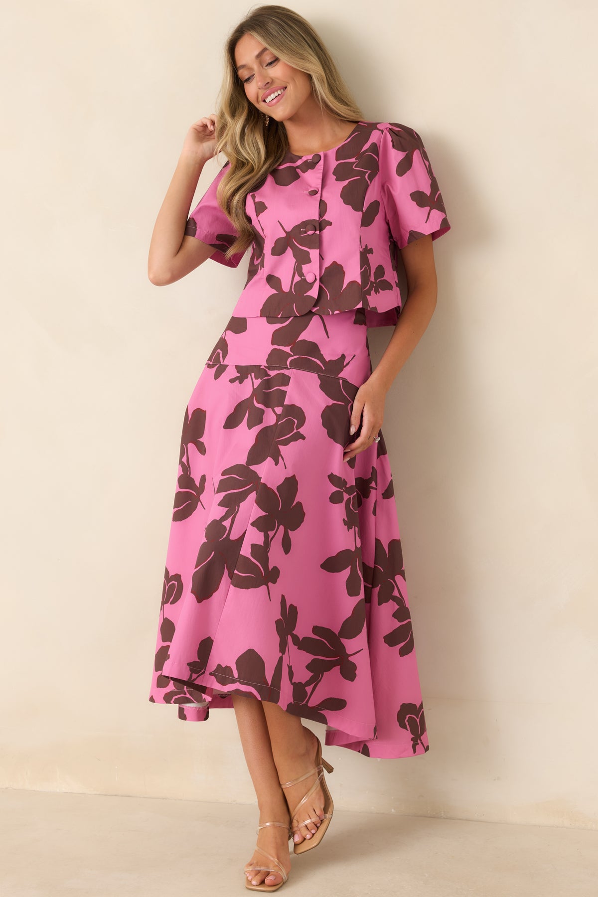 Bright pink top featuring an oversized chocolate brown floral print, round neckline, short puff sleeves, and covered functional buttons down the front.