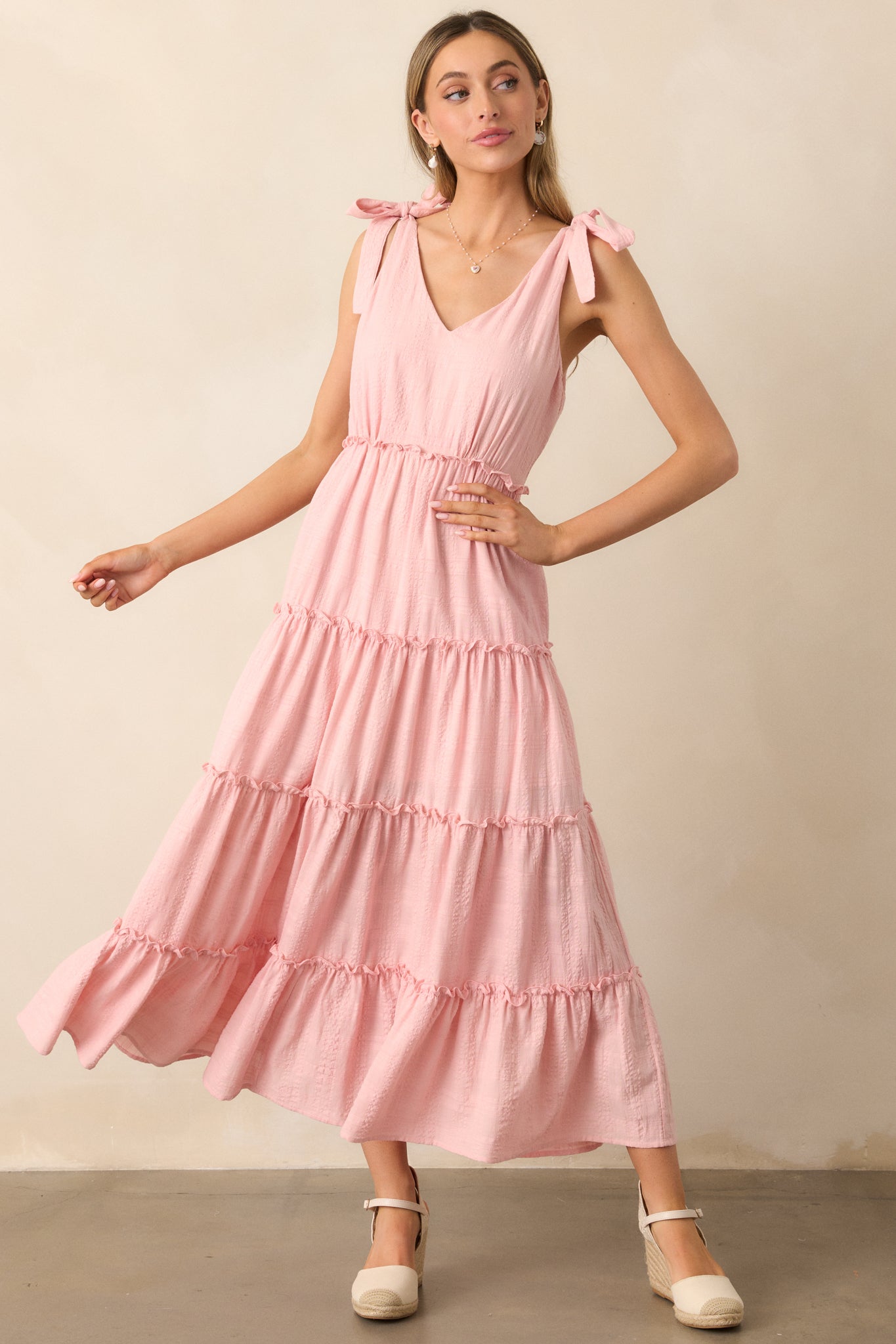 The pink dress with a v-neckline and tiered skirt, self-tie bow straps, and ruffle detailing, designed in lightweight textured fabric for a breezy, feminine look.