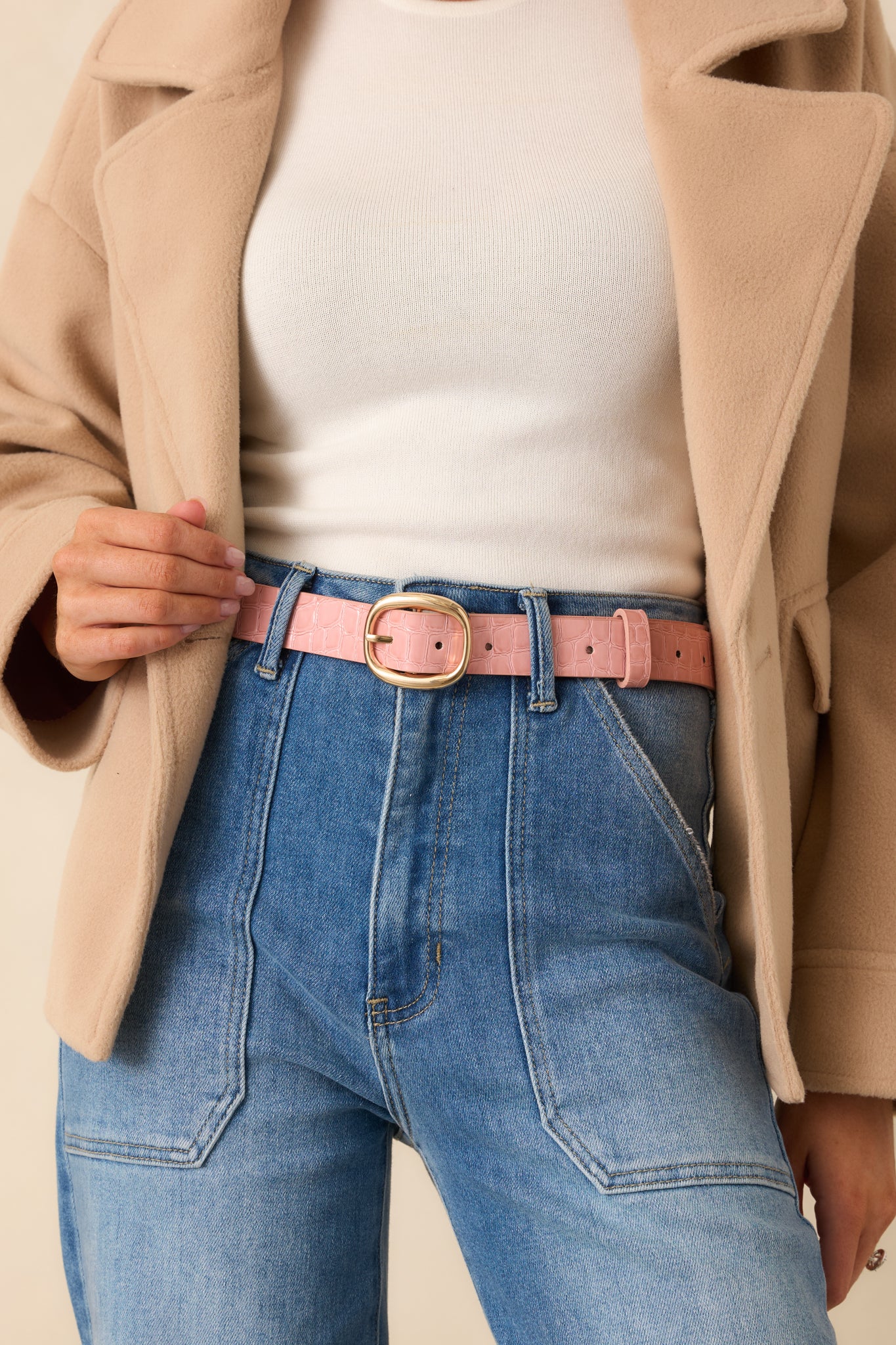 Cropped view of the pink faux leather belt featuring a croc-embossed texture and gold-tone oval buckle.