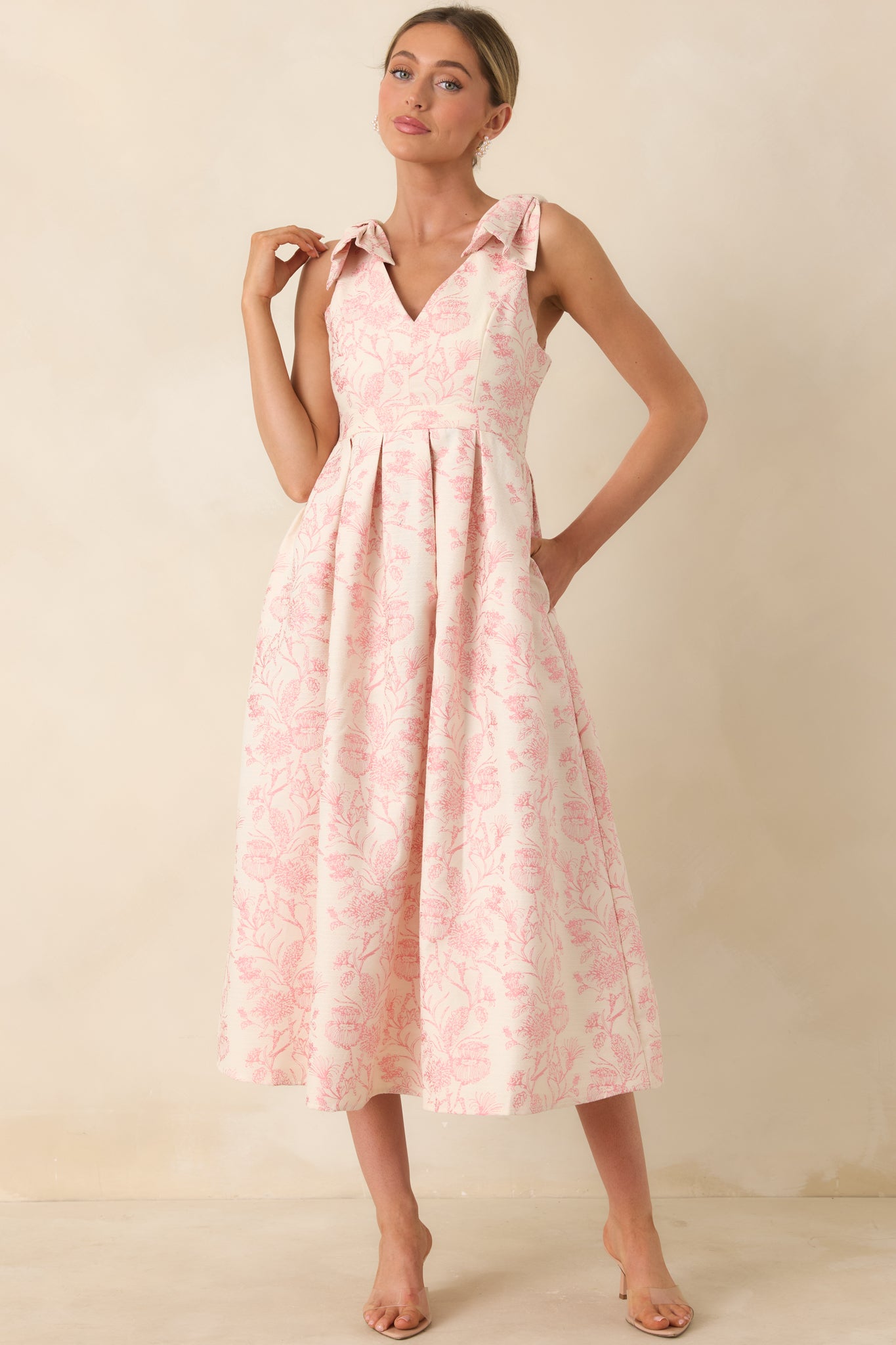 Front view of a pink floral midi dress with bow-tie shoulder straps, V-neckline, and pleated skirt.