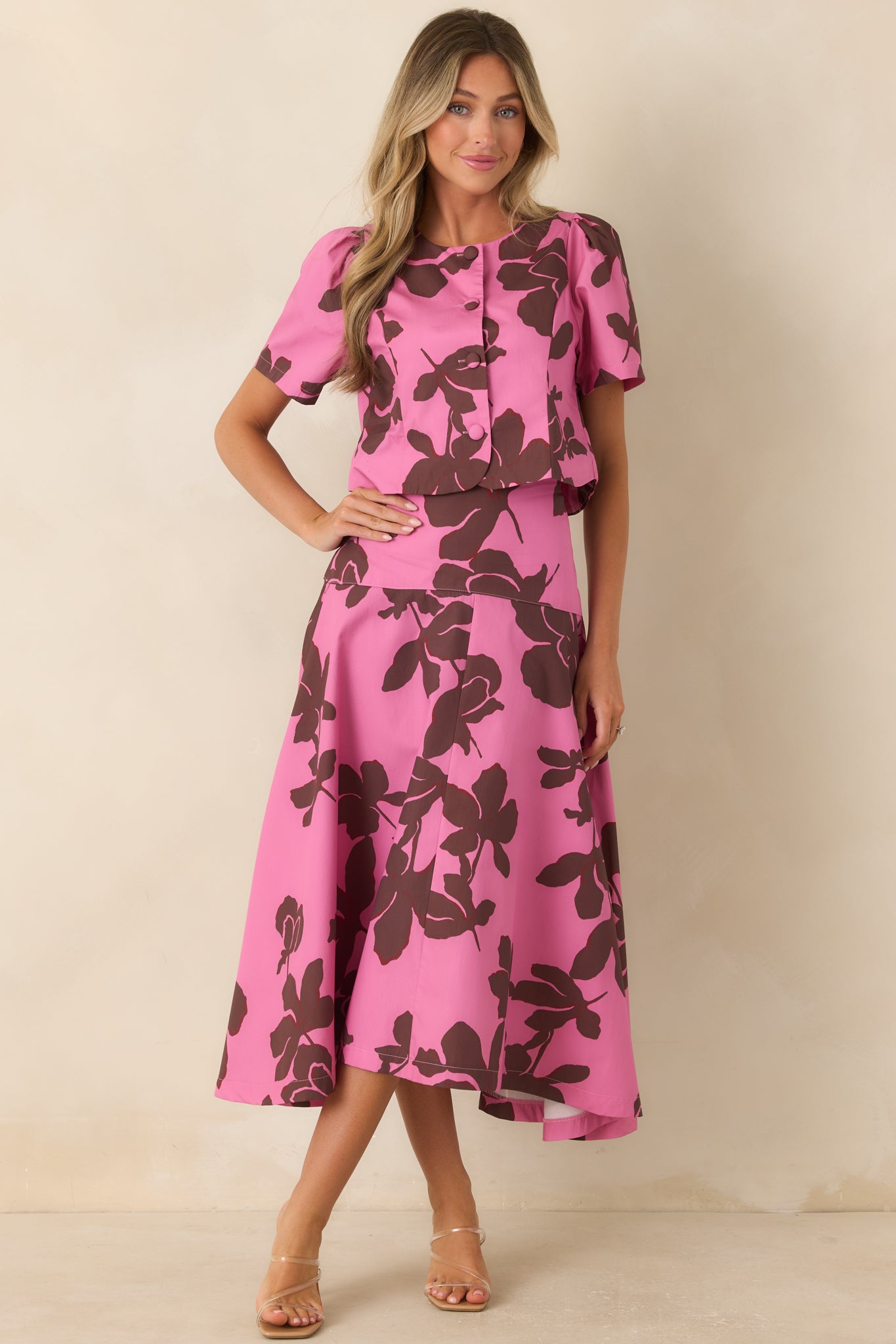 Pink floral top designed with a round neckline, voluminous short puff sleeves, covered buttons, and a refined structured silhouette.