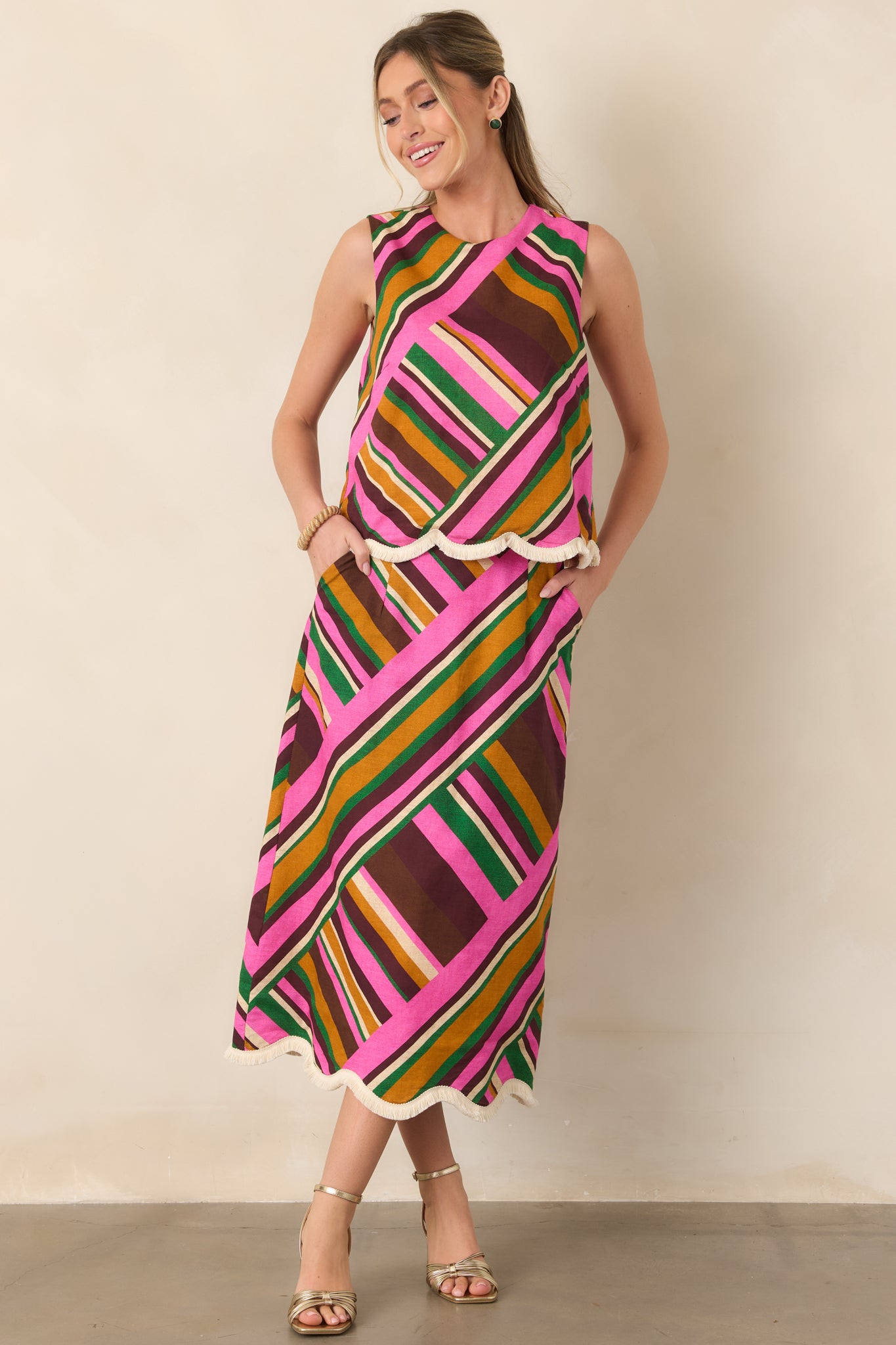 Bold pink geometric stripe top featuring a simple round neckline, flowing sleeveless shape, and playful fringe-trimmed hem.