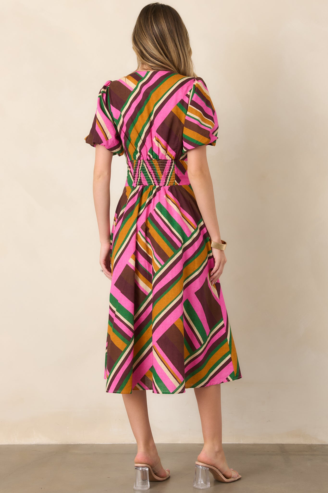 Rear view of the pink geometric striped midi dress, highlighting the puff sleeves, smocked waist, and full flowing skirt.