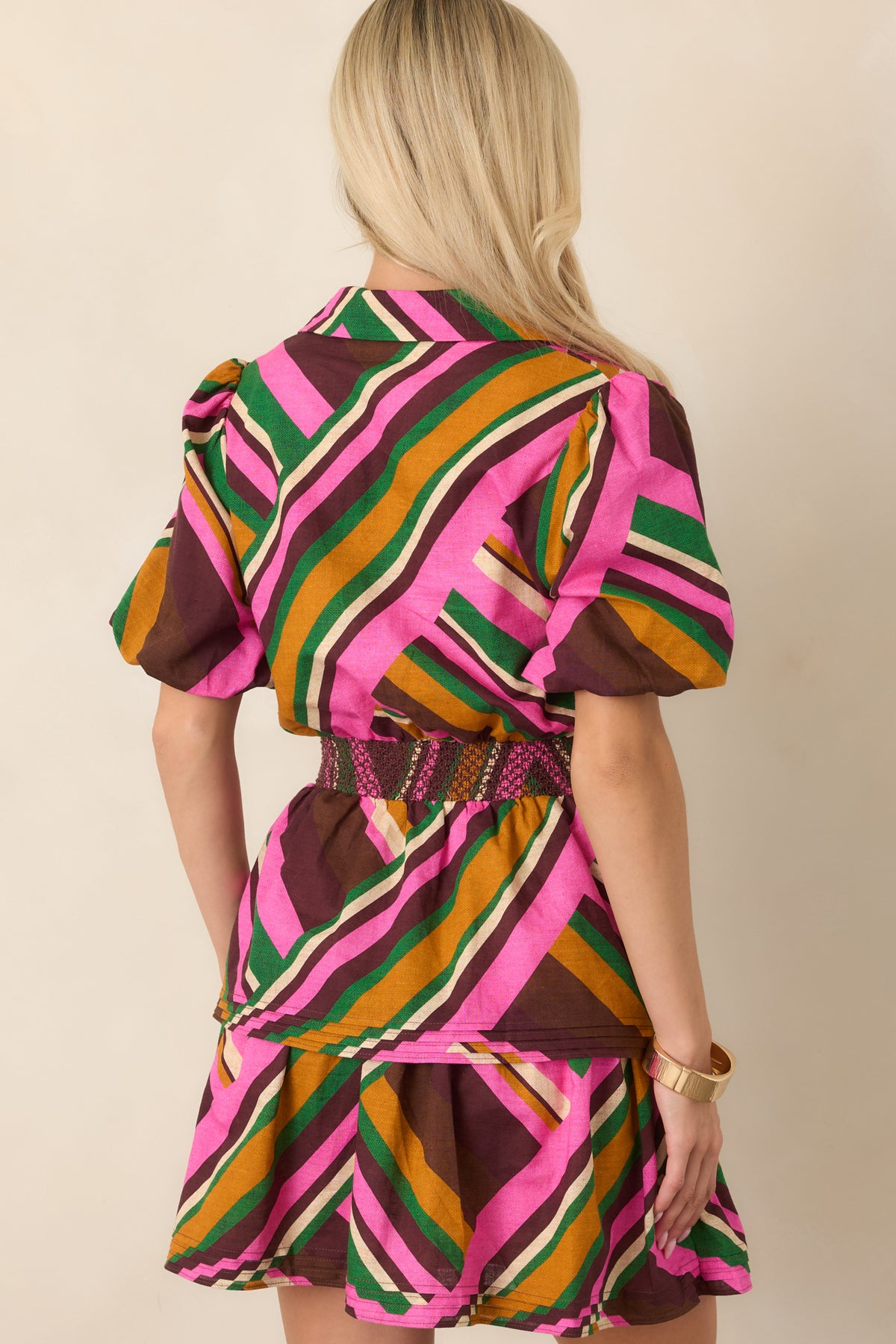 Rear view of the pink geometric striped mini dress, highlighting the puff sleeves, wide smocked waist, tiered skirt, and varied stripe pattern.