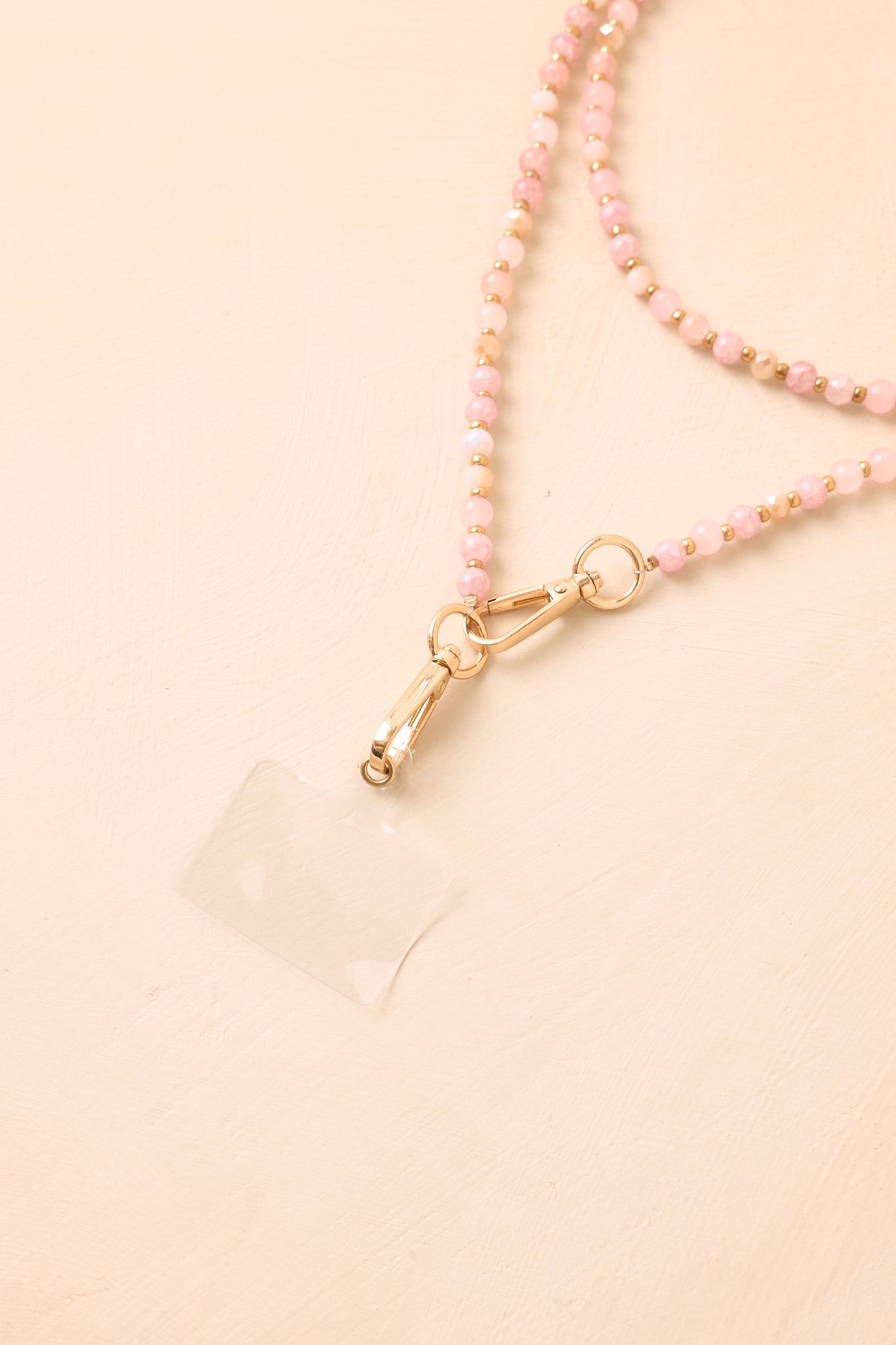 Pink and gold beaded phone lanyard presented on a neutral beige backdrop, showcasing the smooth bead arrangement and refined details.