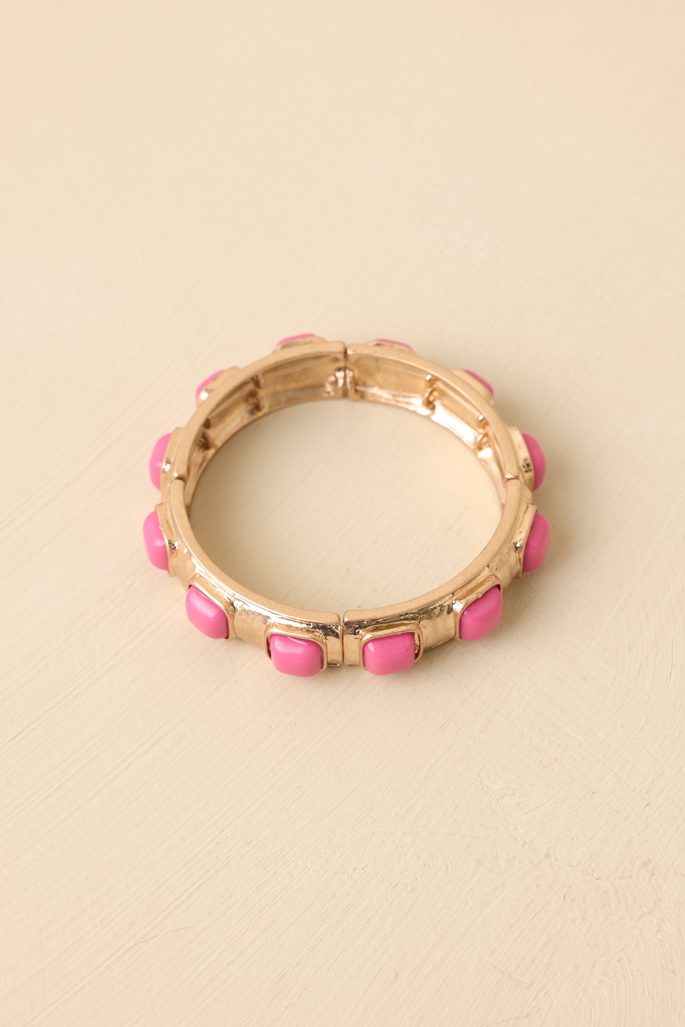 Pink and gold stretch bracelet displayed on a beige background showcasing its segmented design and feminine color contrast.
