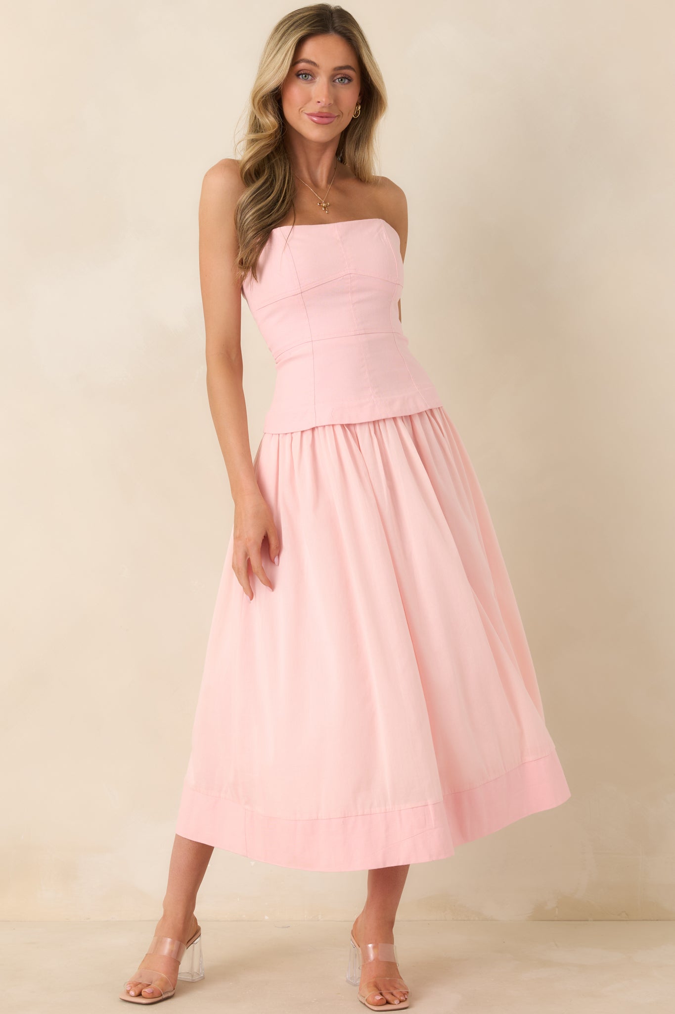 Pink midi dress with a bustier-style paneled bodice, adjustable spaghetti straps, and a flowing gathered skirt with functional pockets.