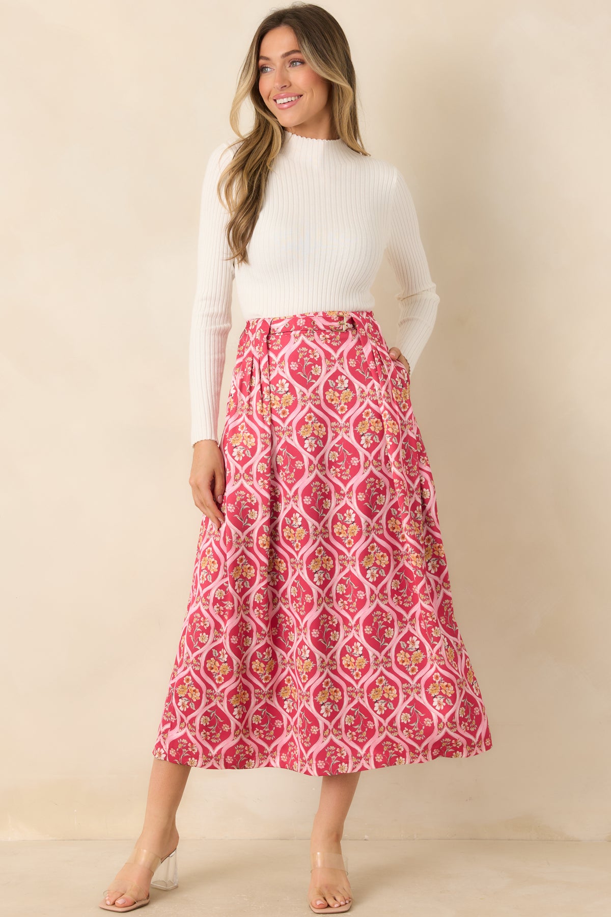Pink printed skirt with a fitted waistband, decorative gold-tone belt buckle, and flowing pleated front.