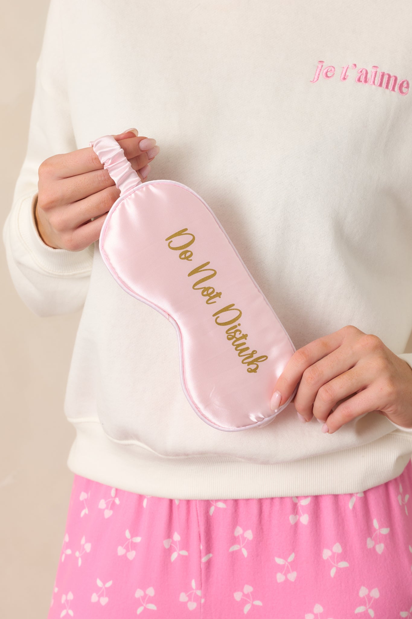 A pink satin eye mask with "Do Not Disturb" in gold lettering across the front, featuring a smooth and luxurious finish.