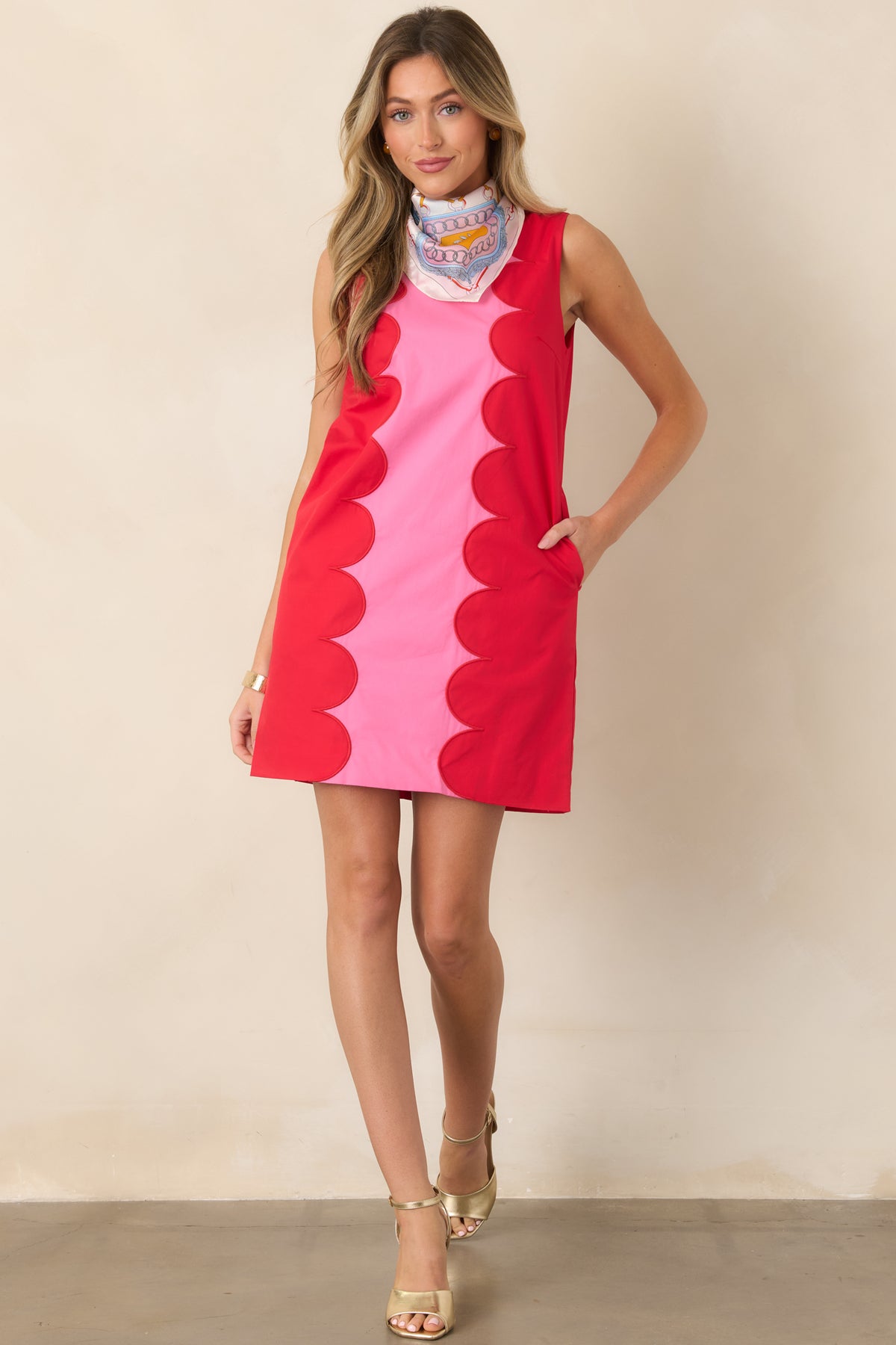 Statement pink mini dress showcasing a sleeveless structured shape and bold red scalloped edging framing the center panel.