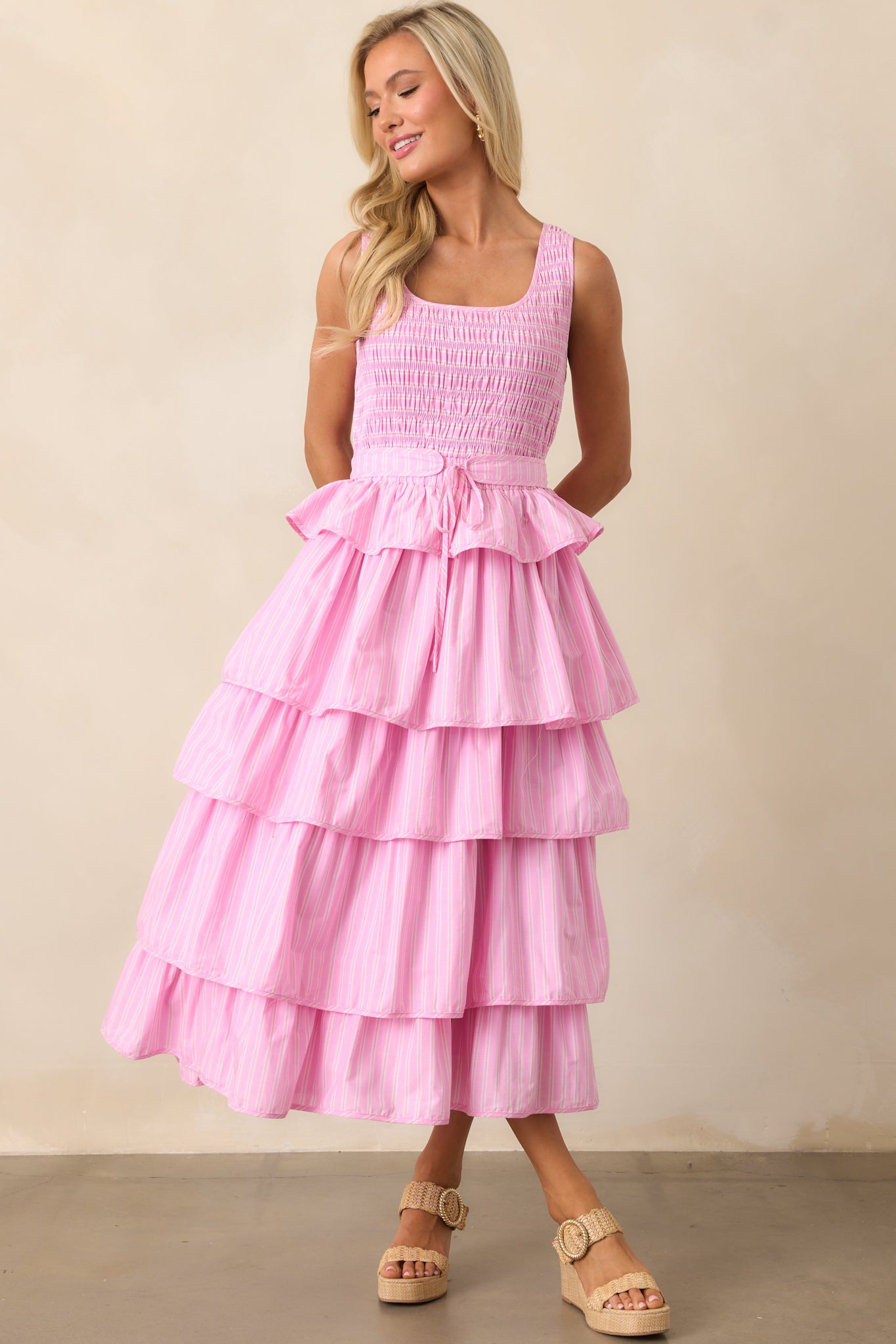 A charming midi dress with a pink stripe print throughout, a structured smocked bodice, and cascading ruffle tiers for added movement.