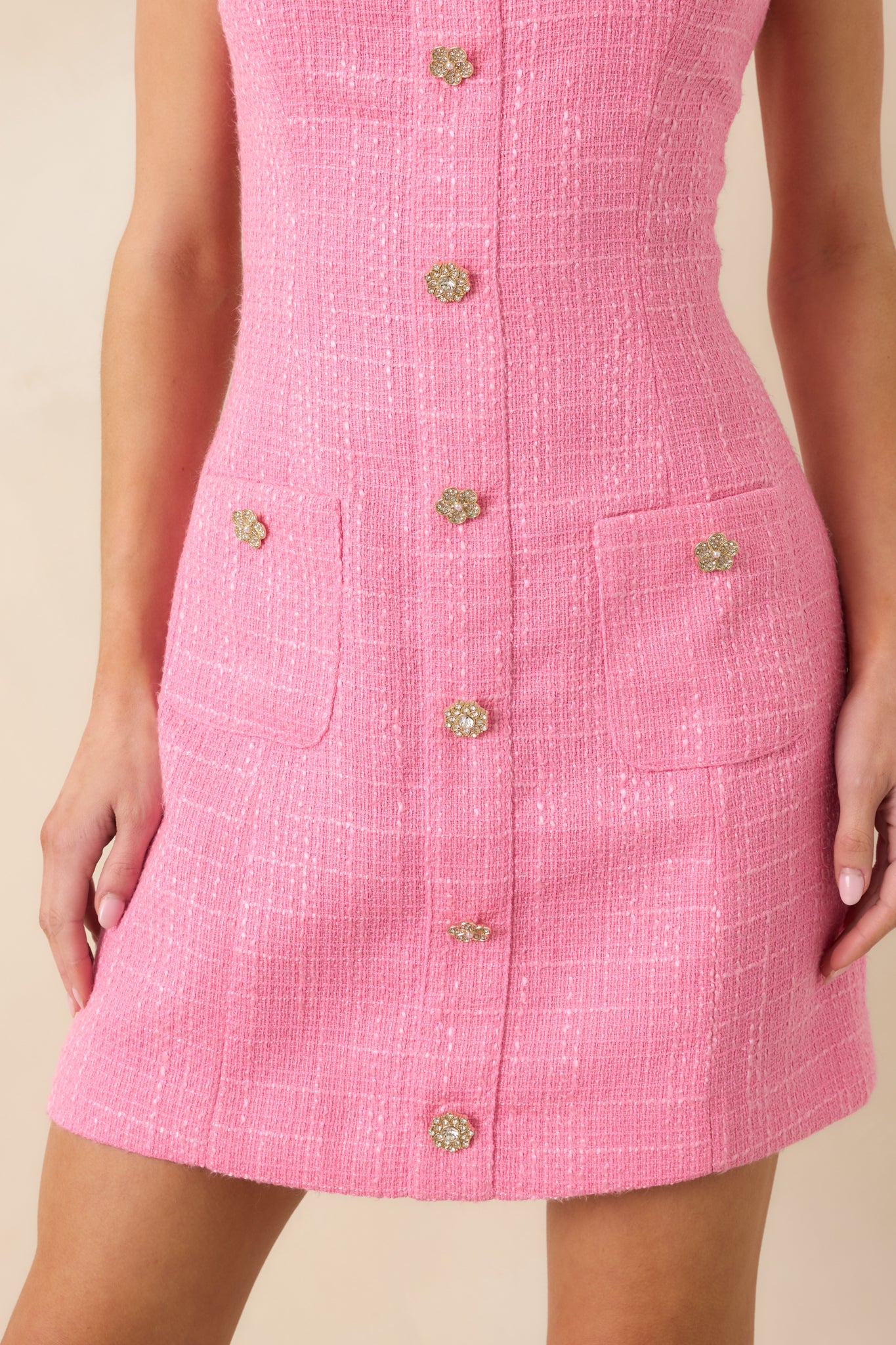 Pink tweed fabric with gold-tone button detail and refined stitching.
