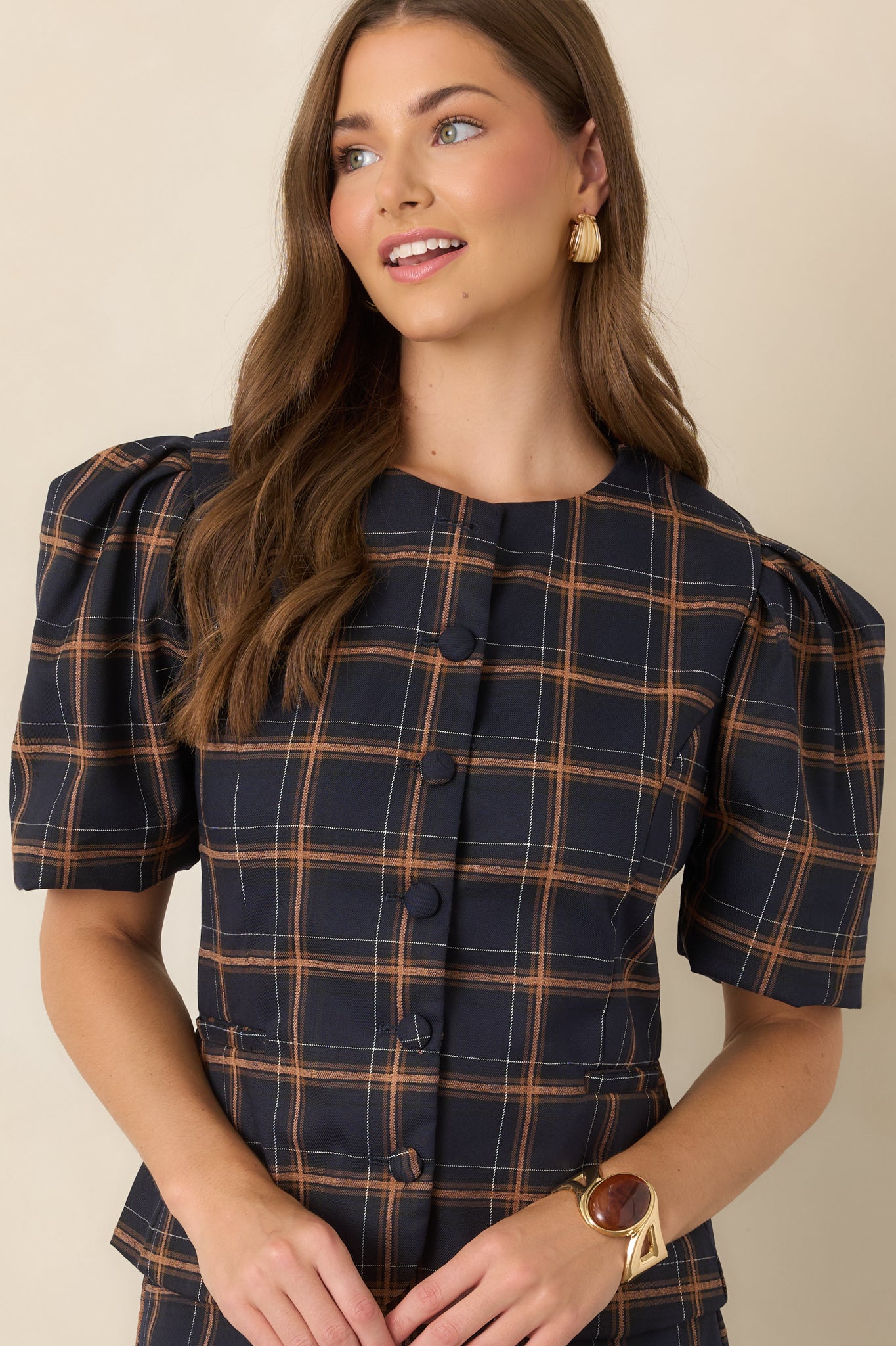 Front view highlighting the top’s fabric-covered buttons, tailored construction, and defined waist against a classic navy plaid backdrop.