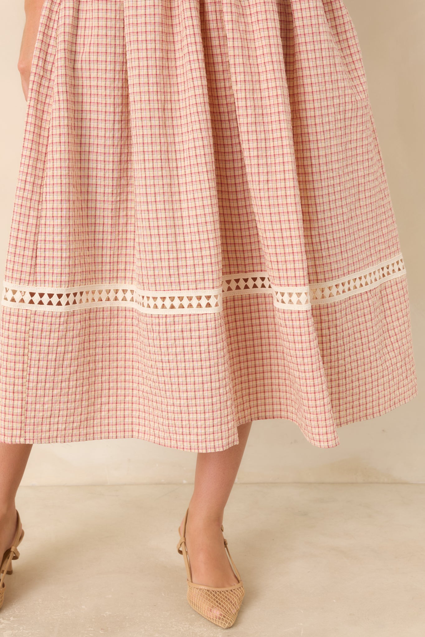 Close-up of the red and beige plaid dress's bottom hem, highlighting the full skirt and decorative crochet inset that adds texture and a delicate finishing touch.