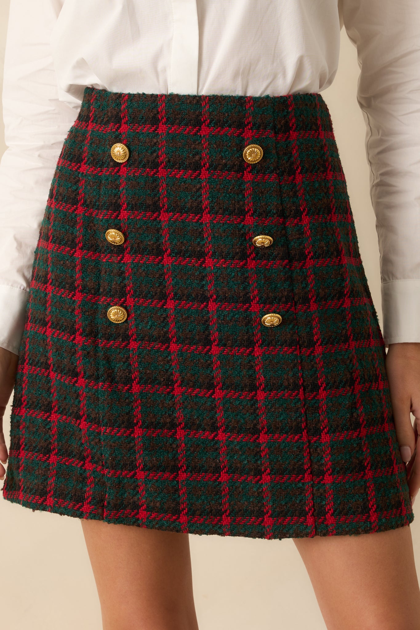 Plaid tweed mini skirt with a high waist and double-breasted gold buttons creating a polished, structured look.