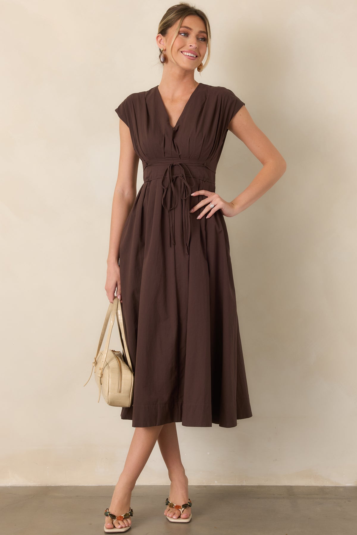 Softly structured midi dress showcasing cap sleeves, pleated detailing, a double strand waist tie, and an easy flowing skirt.