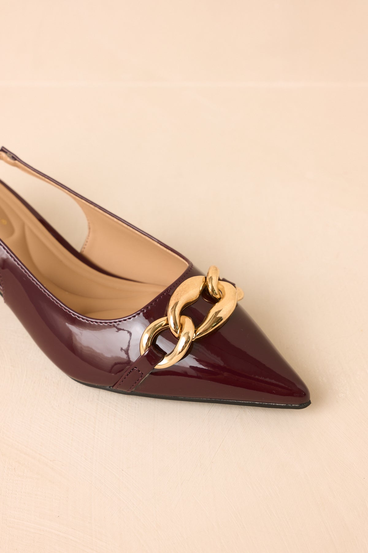 Plum patent heels showcasing the polished finish, pointed silhouette, gold-tone vamp chain, and refined kitten heel.