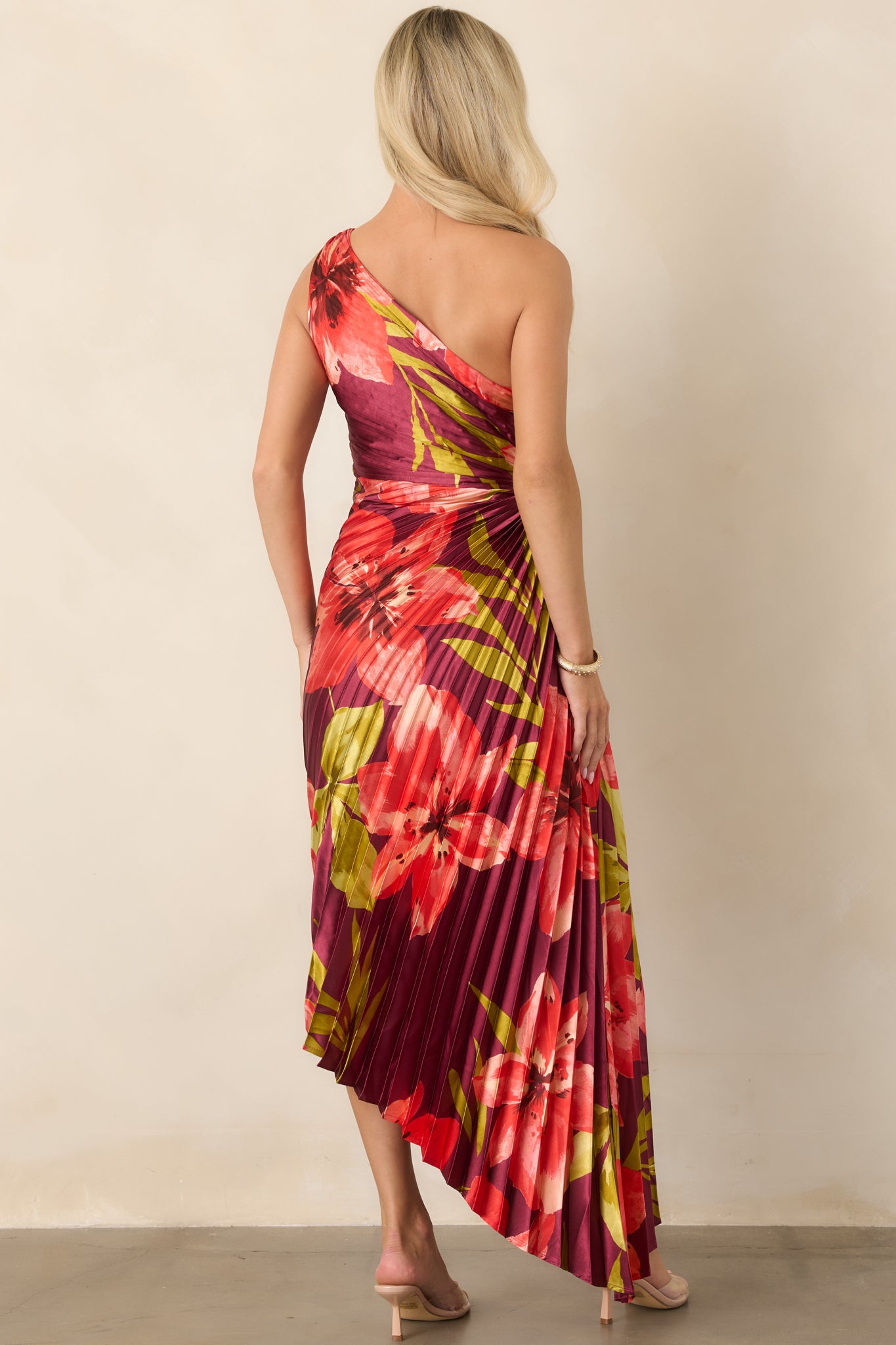 Rear view of the plum satin dress showcasing the pleated construction, one-shoulder design, smooth finish, and asymmetrical hem.