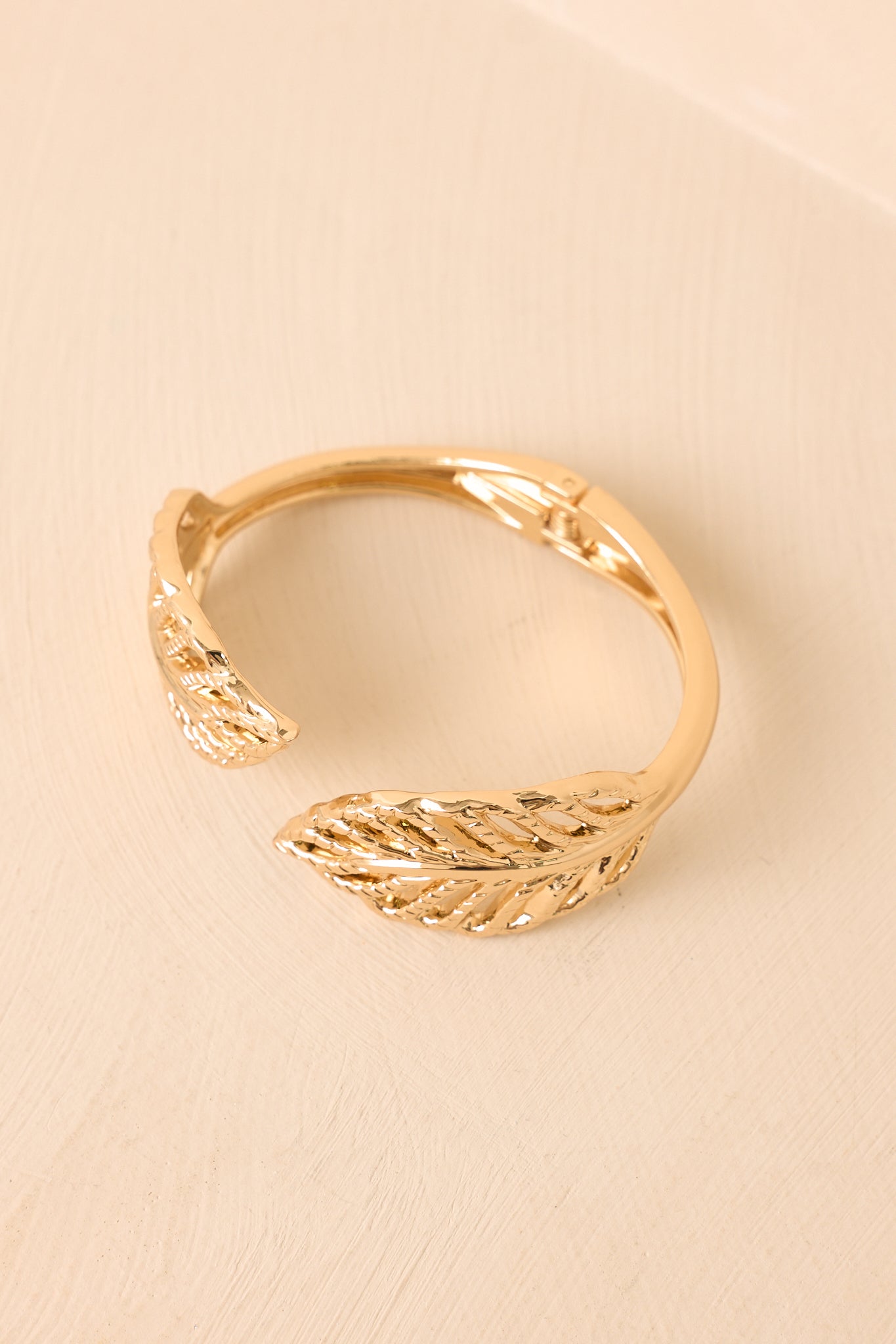 Polished gold statement bracelet with an open design and botanical-inspired accents displayed on a beige backdrop.