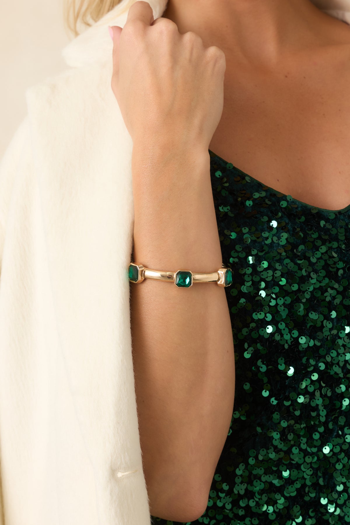 Polished gold-tone bracelet accented with rich green gemstones and reflective faceted surfaces.