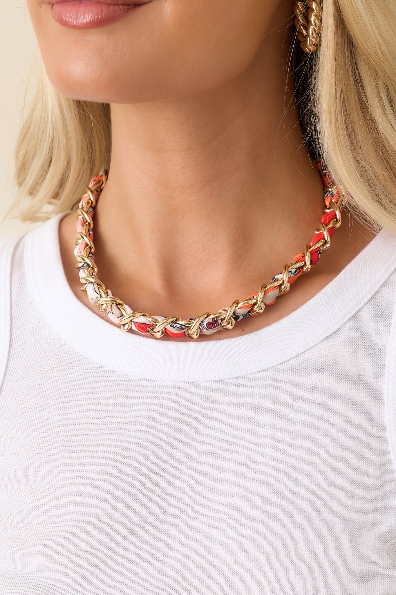 Detailed view of the polished gold-tone links intricately woven with orange patterned scarf fabric, highlighting the textured craftsmanship and dimensional design.