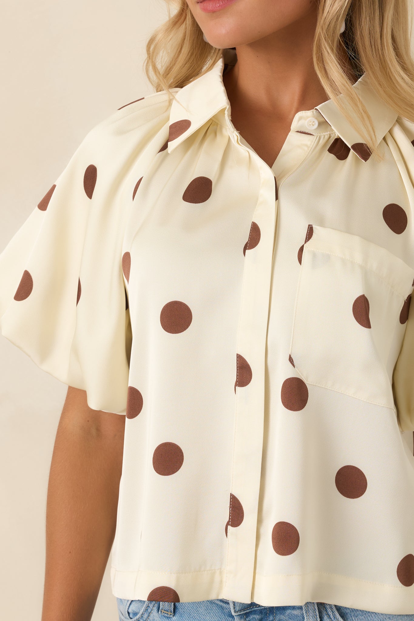 Detailed view of the polka dot fabric, structured collar, concealed buttons, and gathered shoulder details.