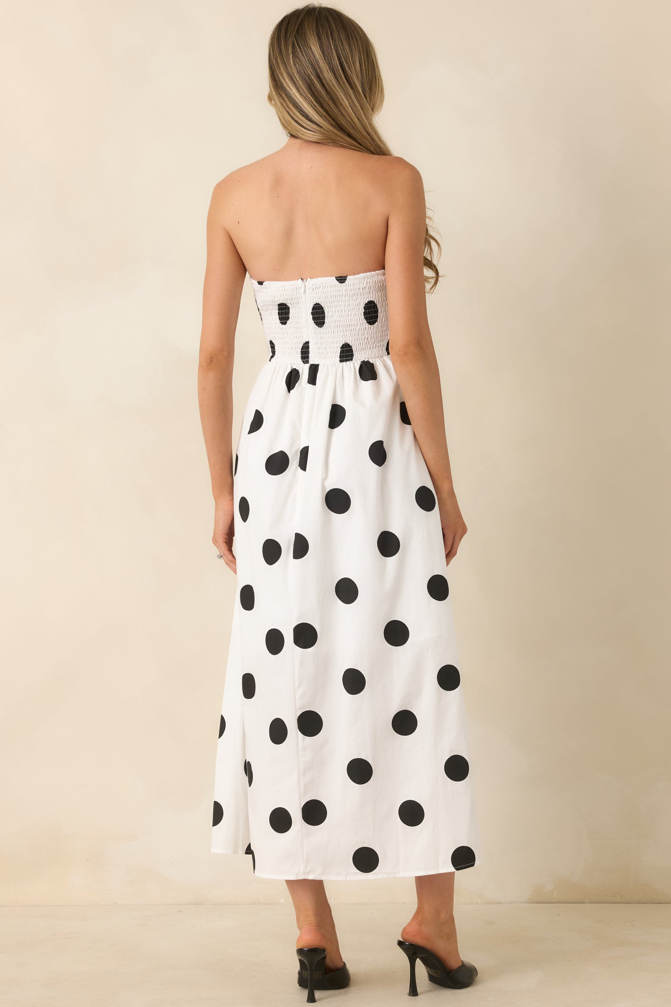 Rear view of the black polka dot midi dress highlighting the smocked back panel, concealed zipper, strapless neckline, and flowing A-line skirt.