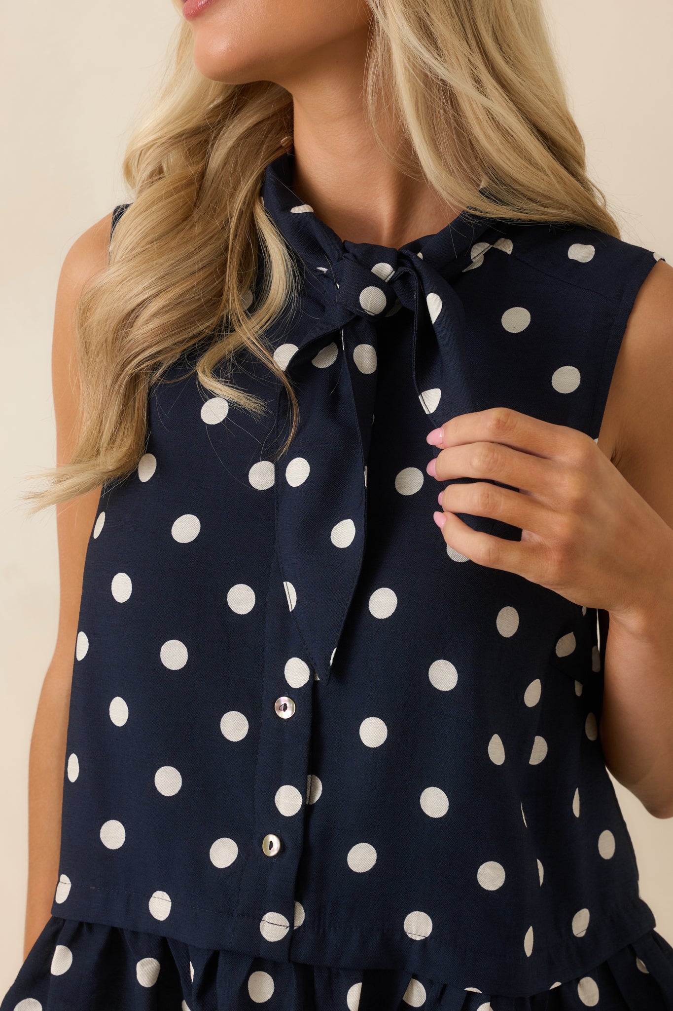 Close-up detail of the polka dot blouse highlighting the tie neckline, button accents, and ruffled peplum trim.