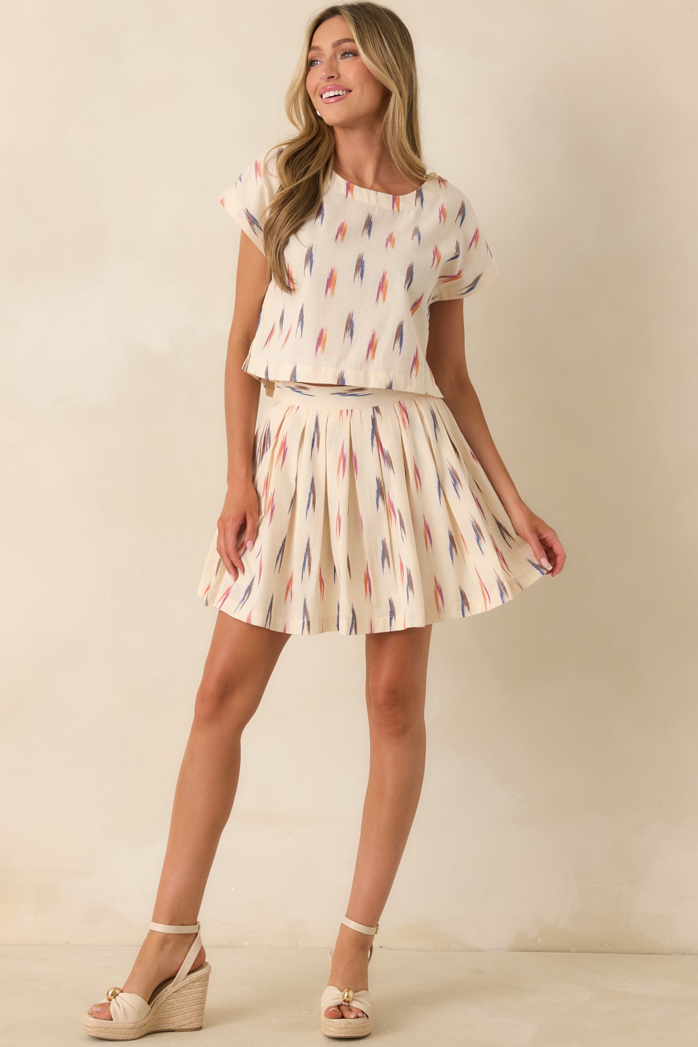 Printed ivory mini skirt with soft pleats and a playful colorful pattern.